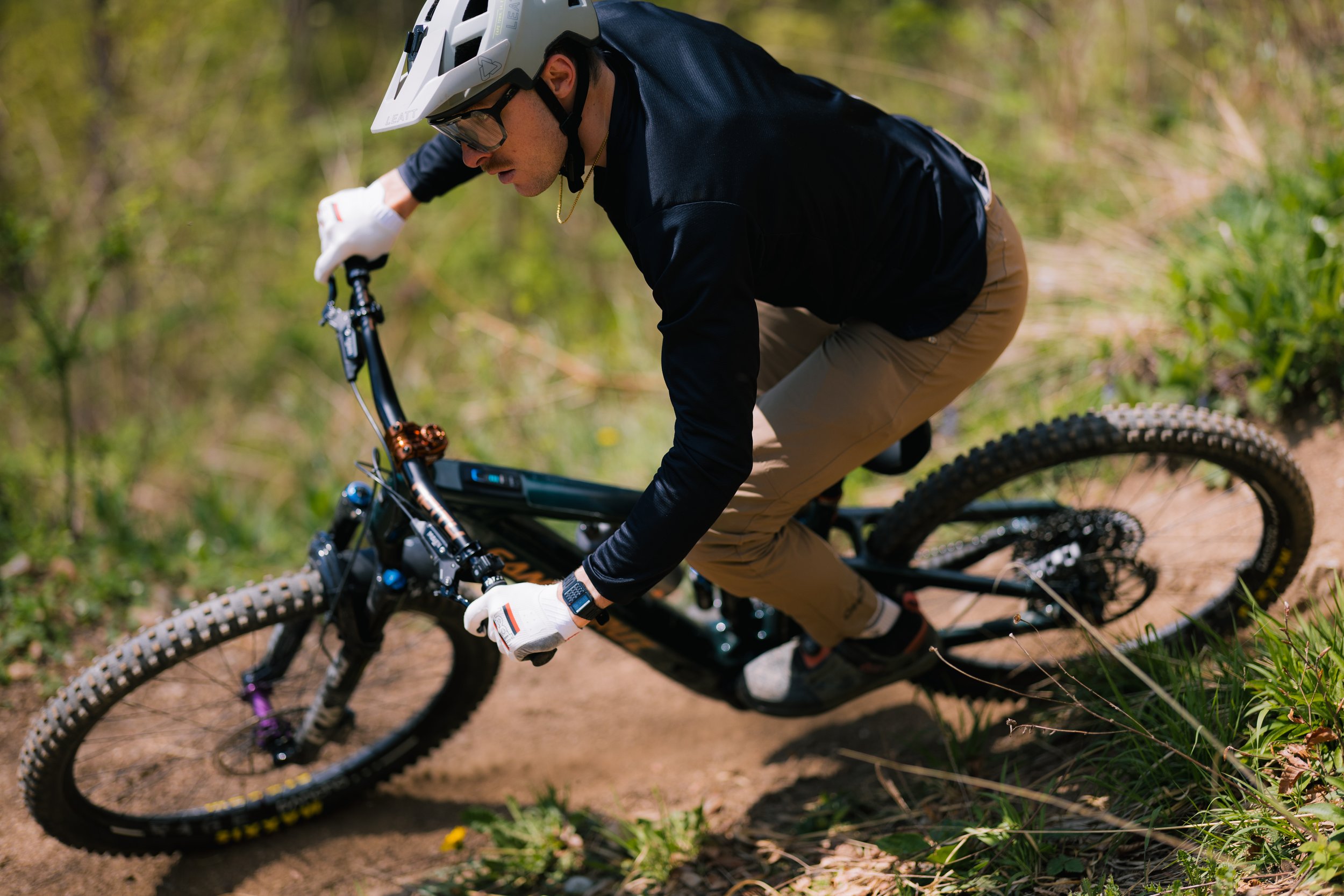 Eine Person fährt mit einem Mountainbike auf einem Waldpfad. Die Person trägt einen Helm, Handschuhe und Sportkleidung.