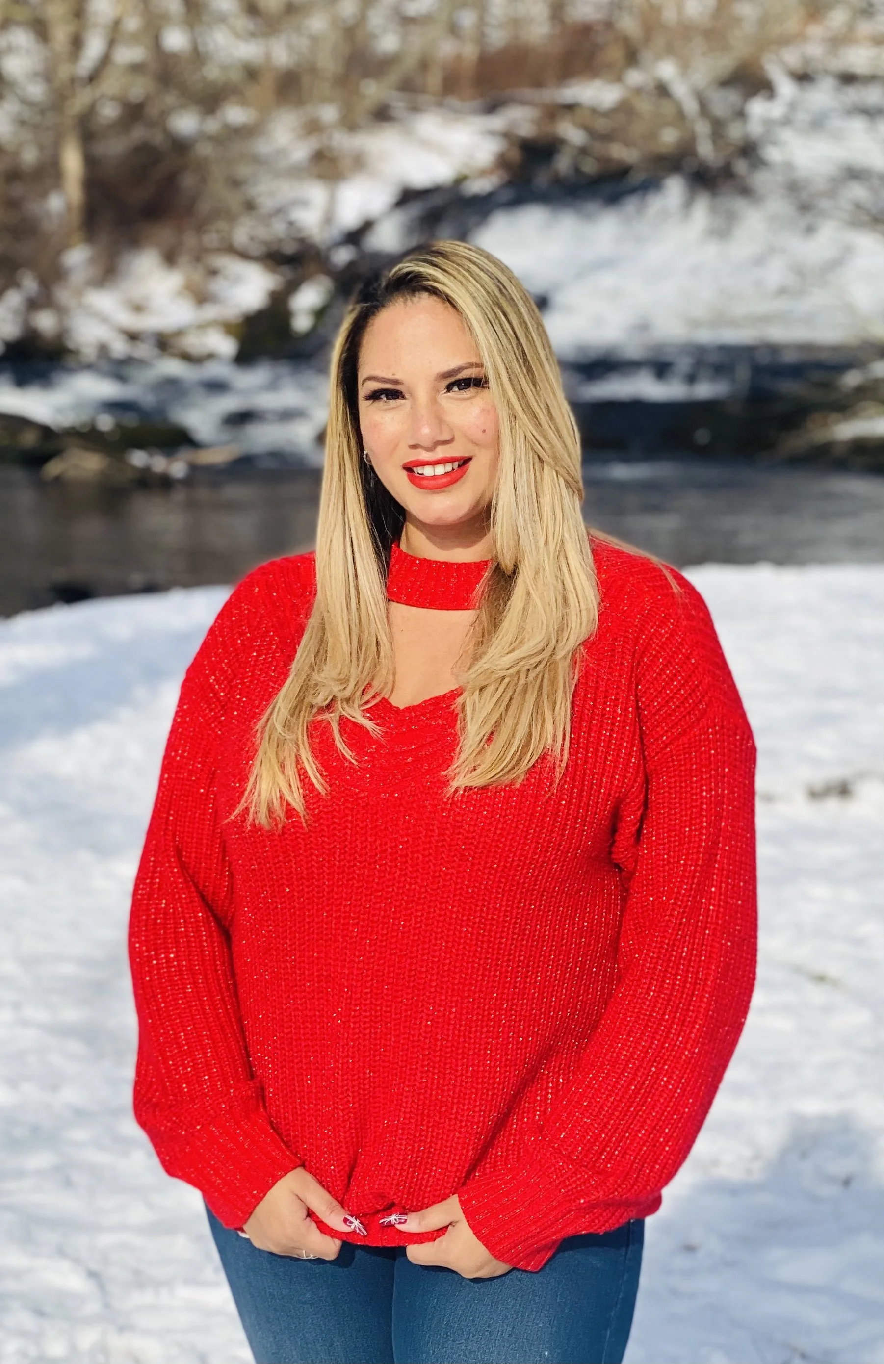 A woman in a red sweater with snow and a river in the background during winter.