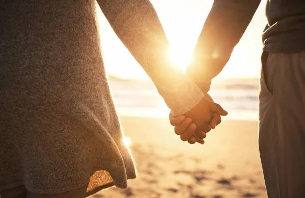 A couple holding hands and connecting with each other on a peaceful beach during sunset.