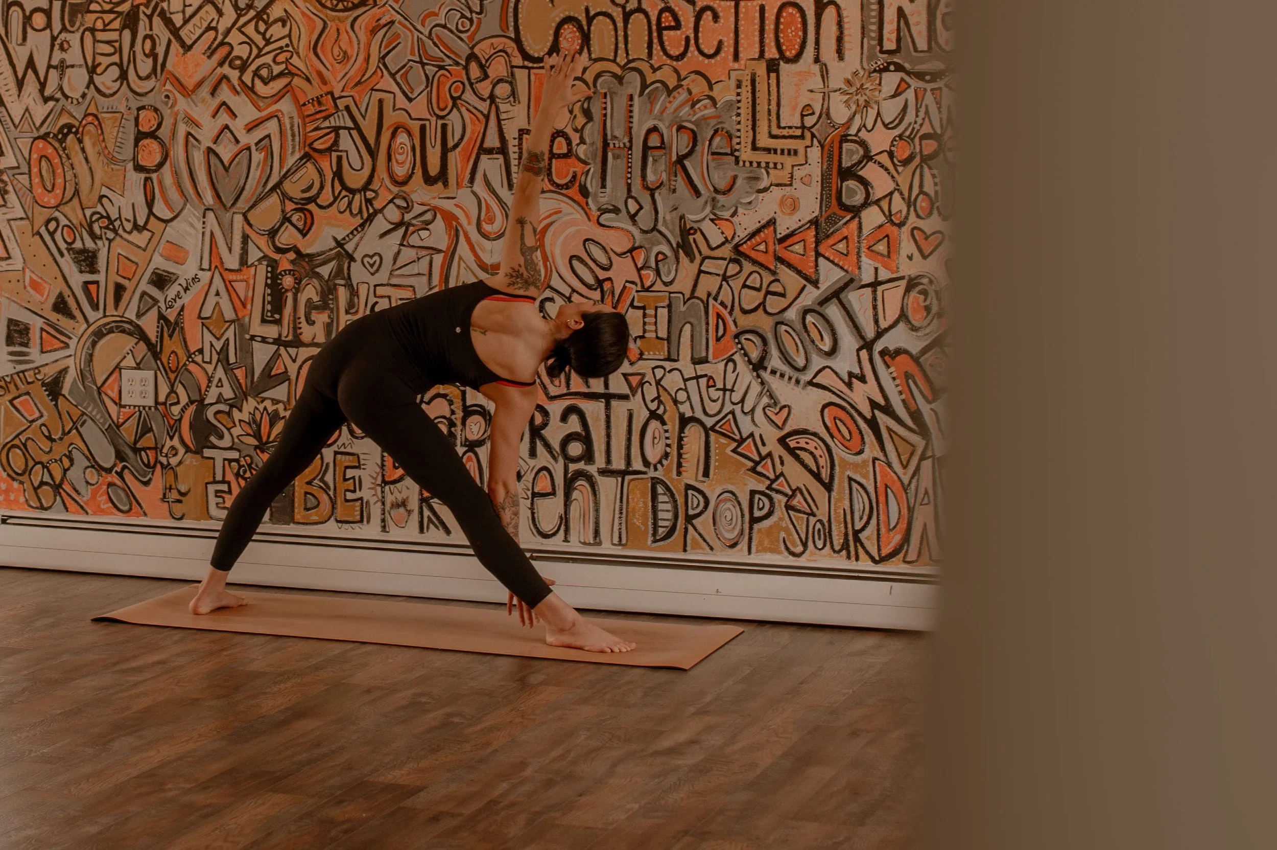 A woman practicing yoga on a mat in a studio with colorful wall art featuring words and symbols.