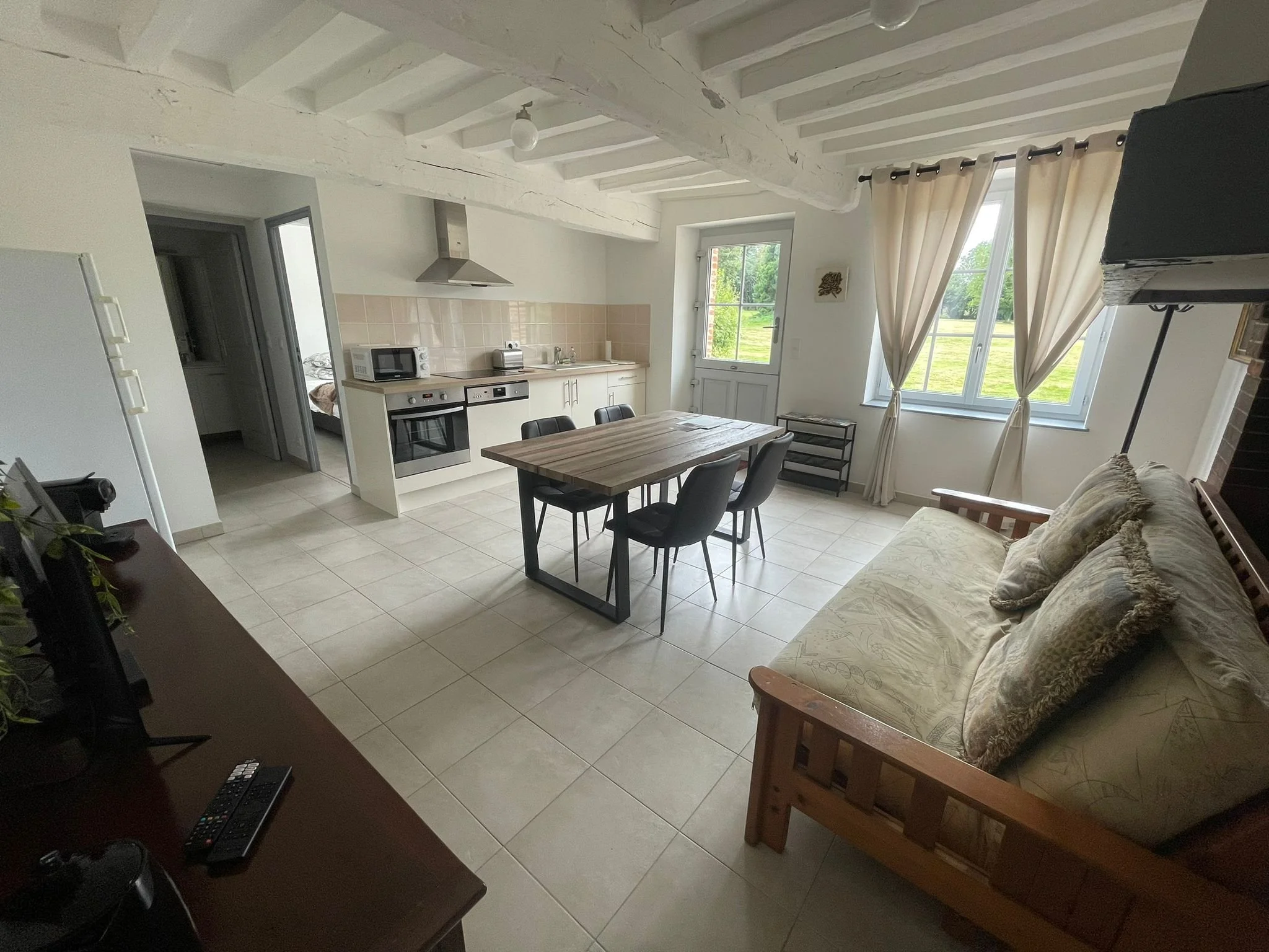 Intérieur d'une cuisine ouverte avec table en bois, canapé et grande fenêtre avec rideaux.