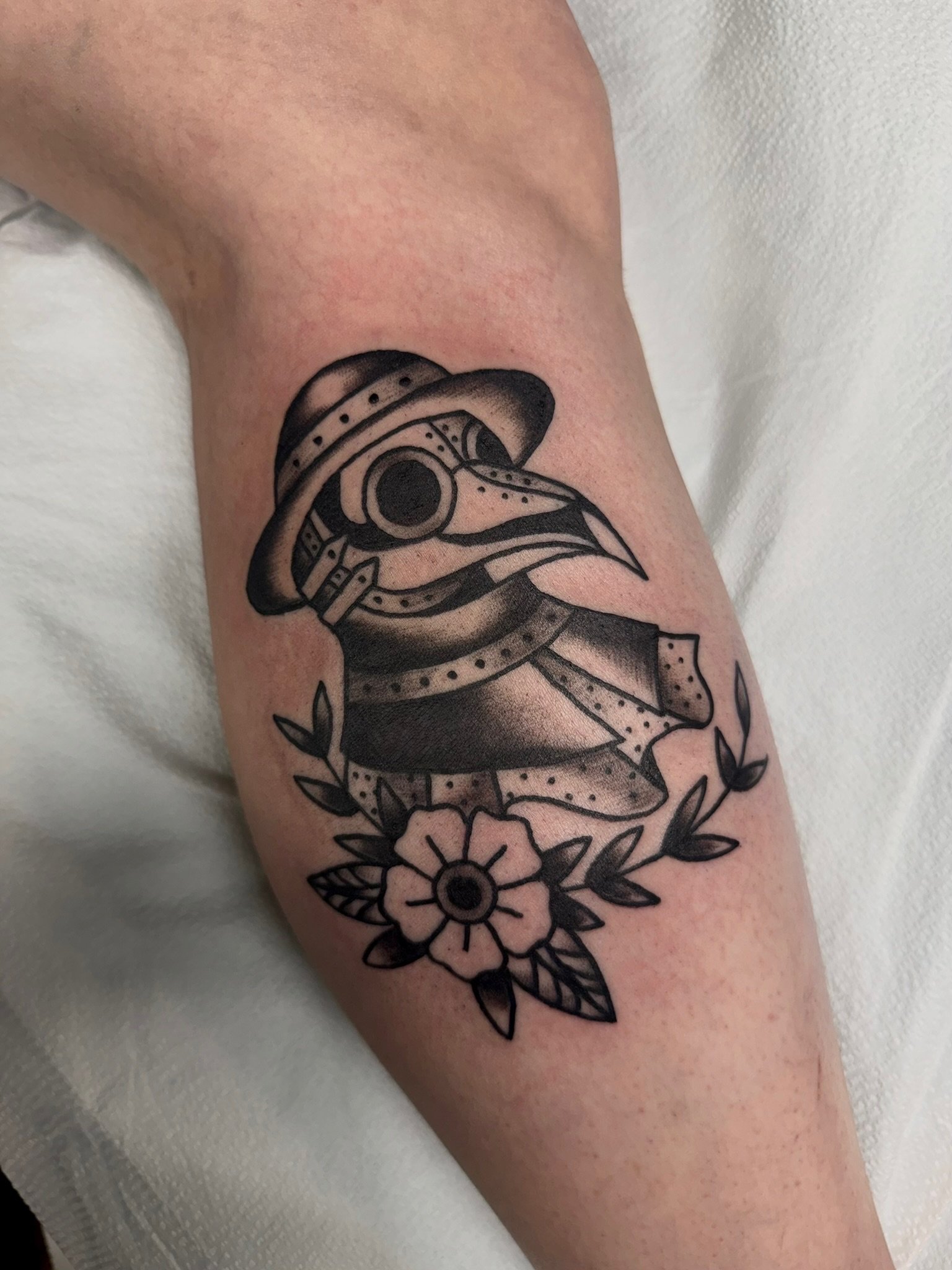 Traditional tattoo of a plague doctor in black and gray ink by Leah Fries, located at Moth to a Flame Tattoo, Old Colorado City
