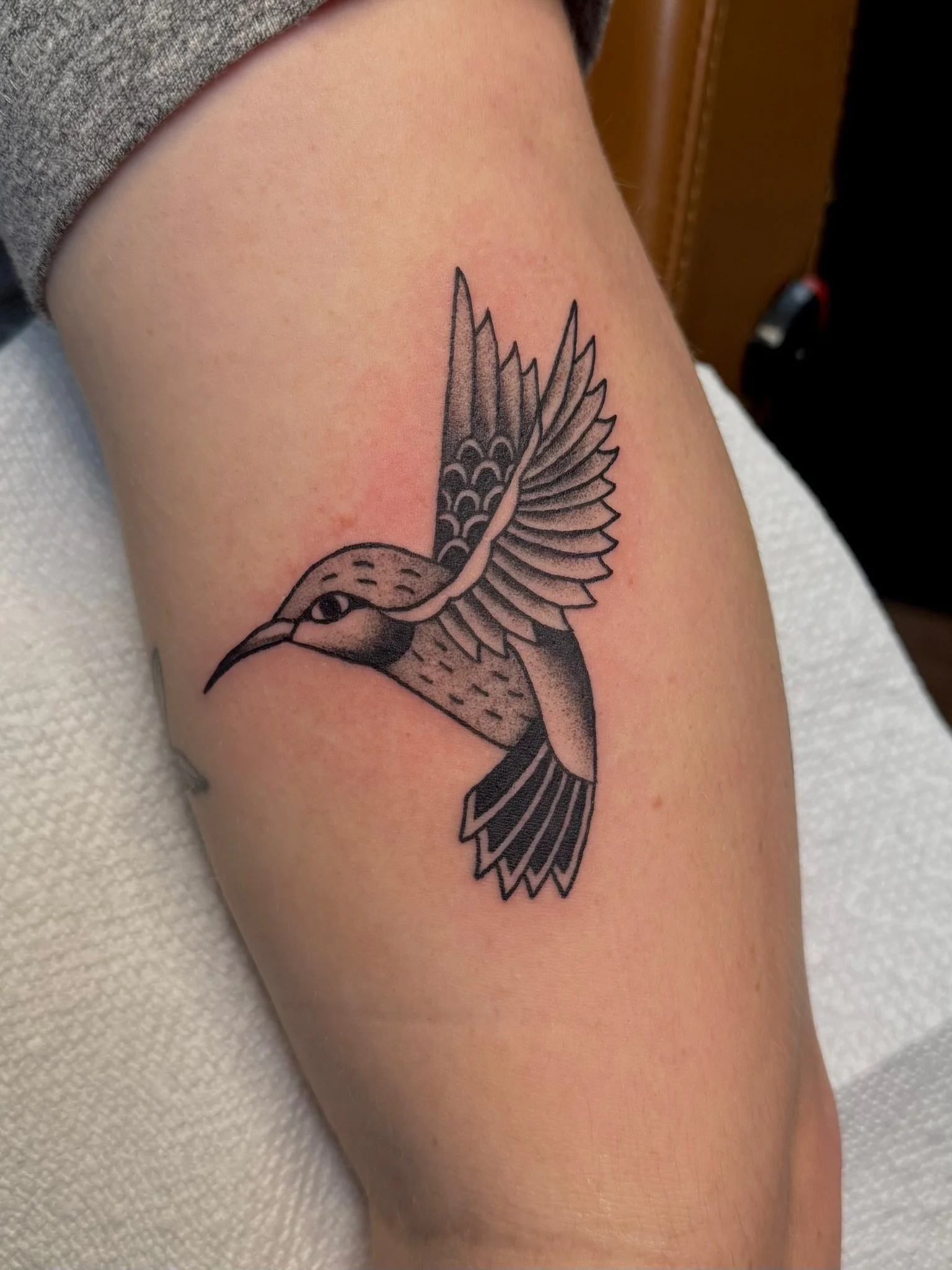 Traditional tattoo of a hummingbird in black and gray ink by Leah Fries, located at Moth to a Flame Tattoo, Colorado Springs