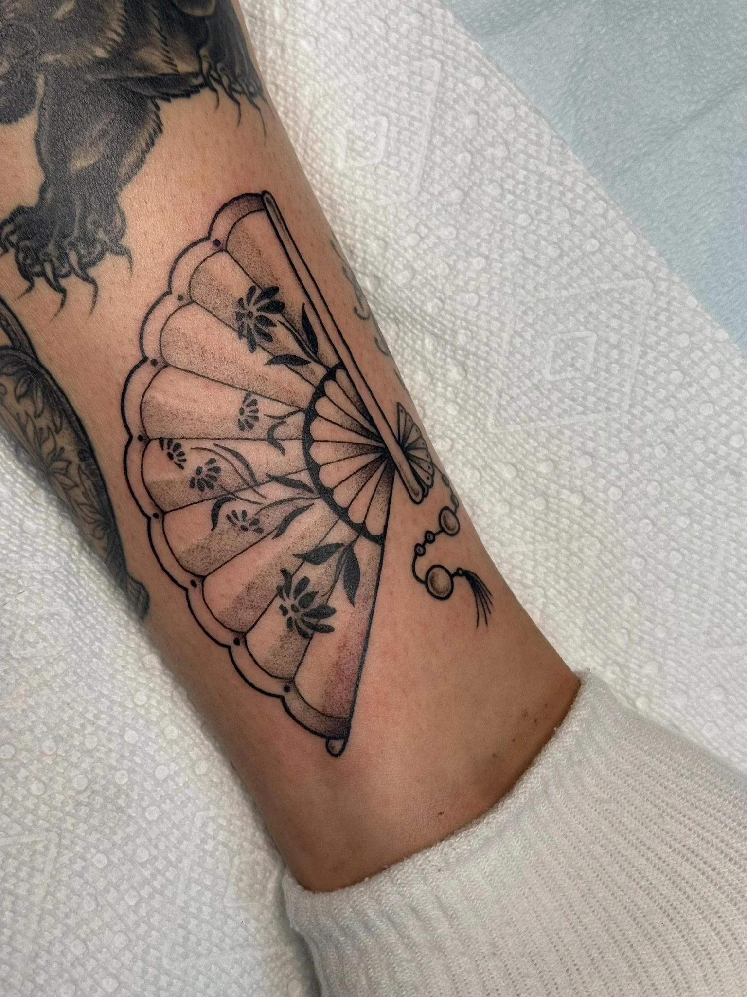 Fine line tattoo of a hand fan in black and gray ink by Leah Fries, located at Moth to a Flame Tattoo, Colorado Springs