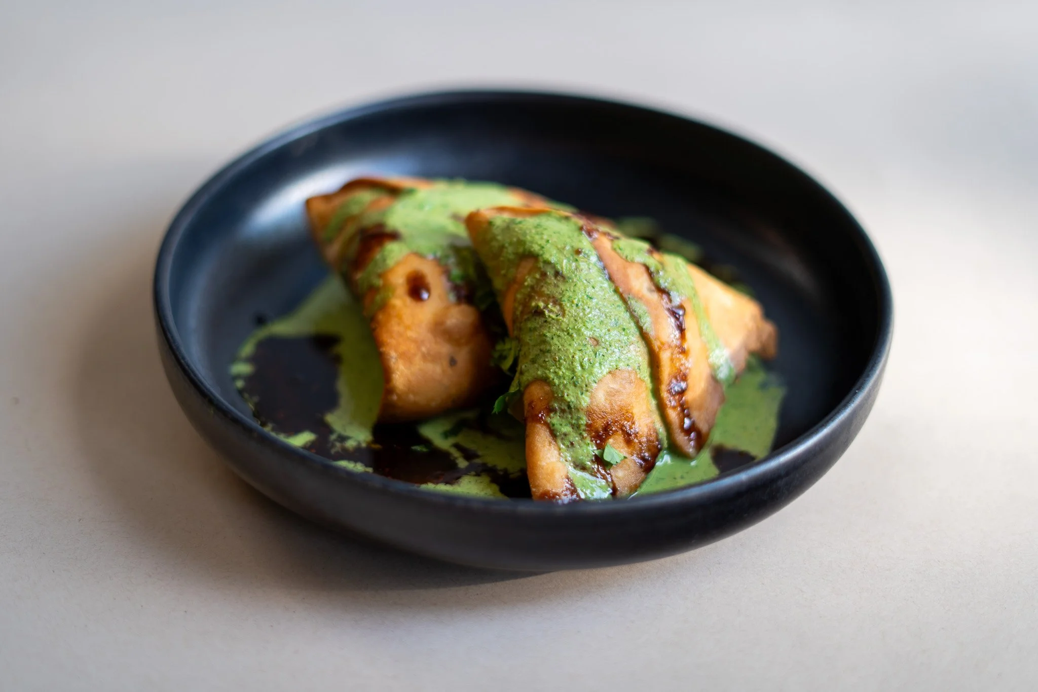 Empanada frita en plato negro con salsa verde y balsámica