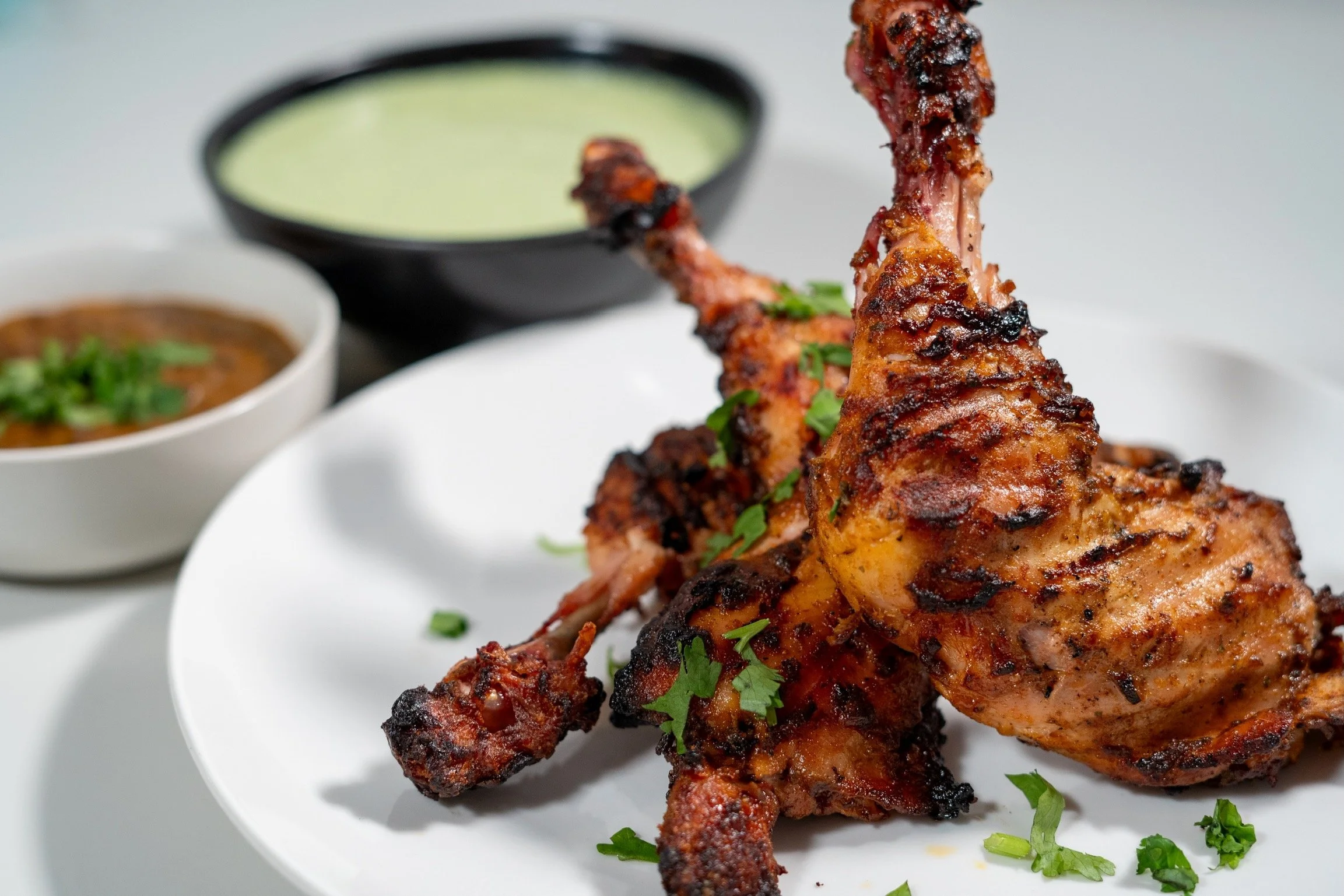 Pollo a la parrilla con cilantro en un plato blanco acompañado de salsas en recipientes negros y blancos.