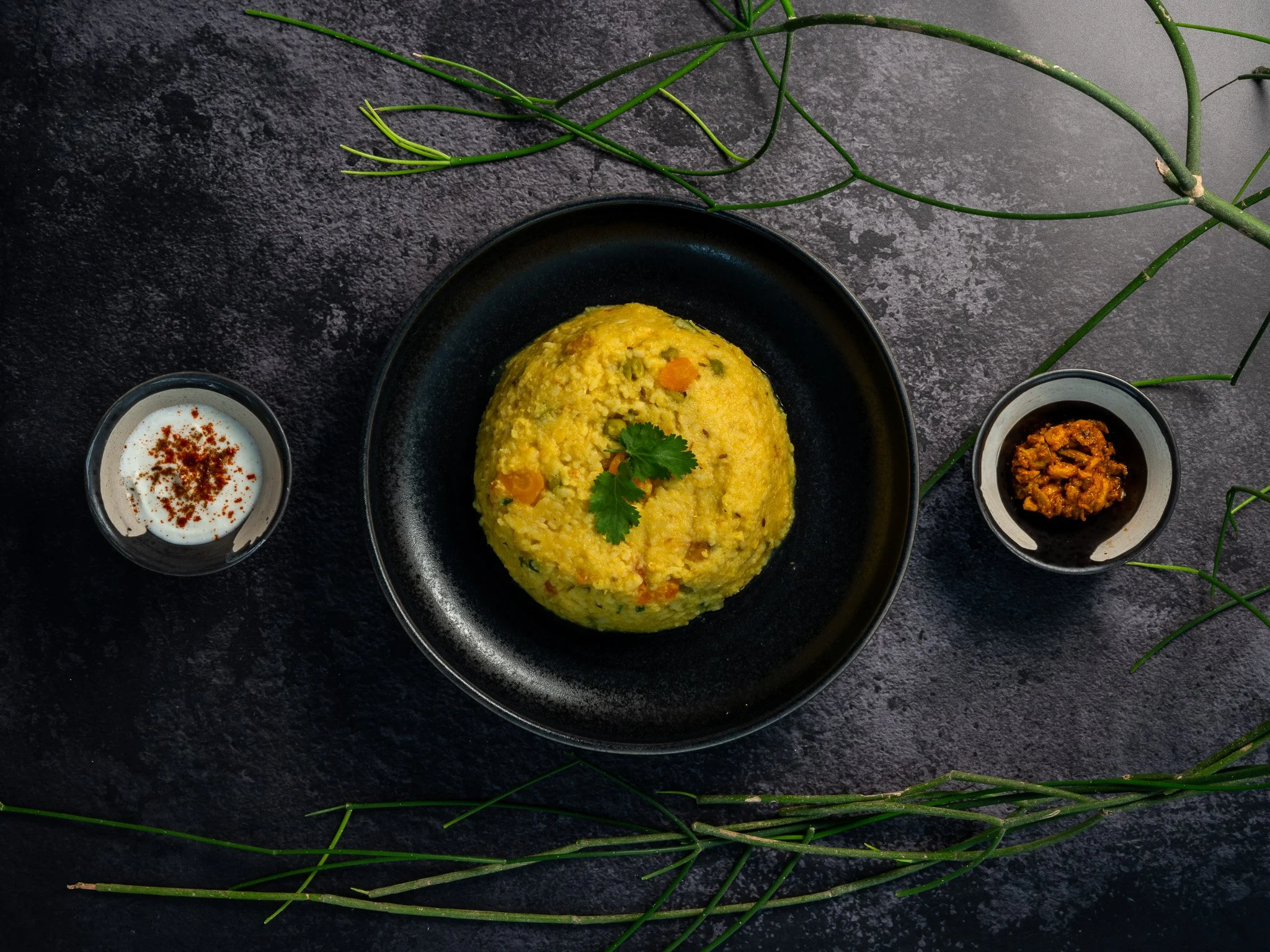 Plato de arroz amarillo con verduras, acompañado de crema con especias y un guiso en pequeños recipientes.