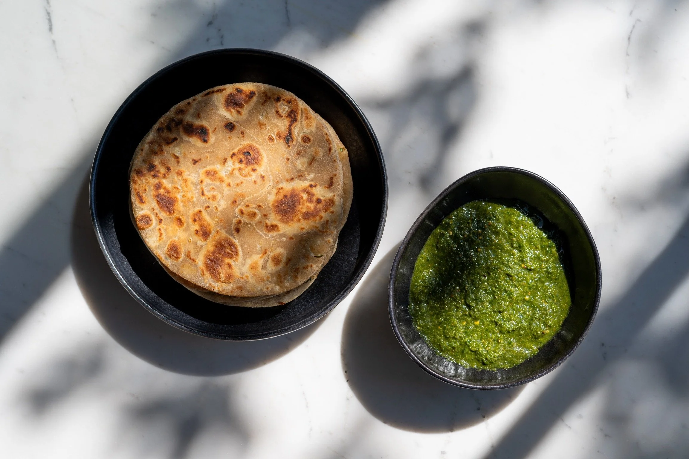 Una tortilla de harina y un recipiente con salsa verde en platos negros sobre una mesa de mármol.