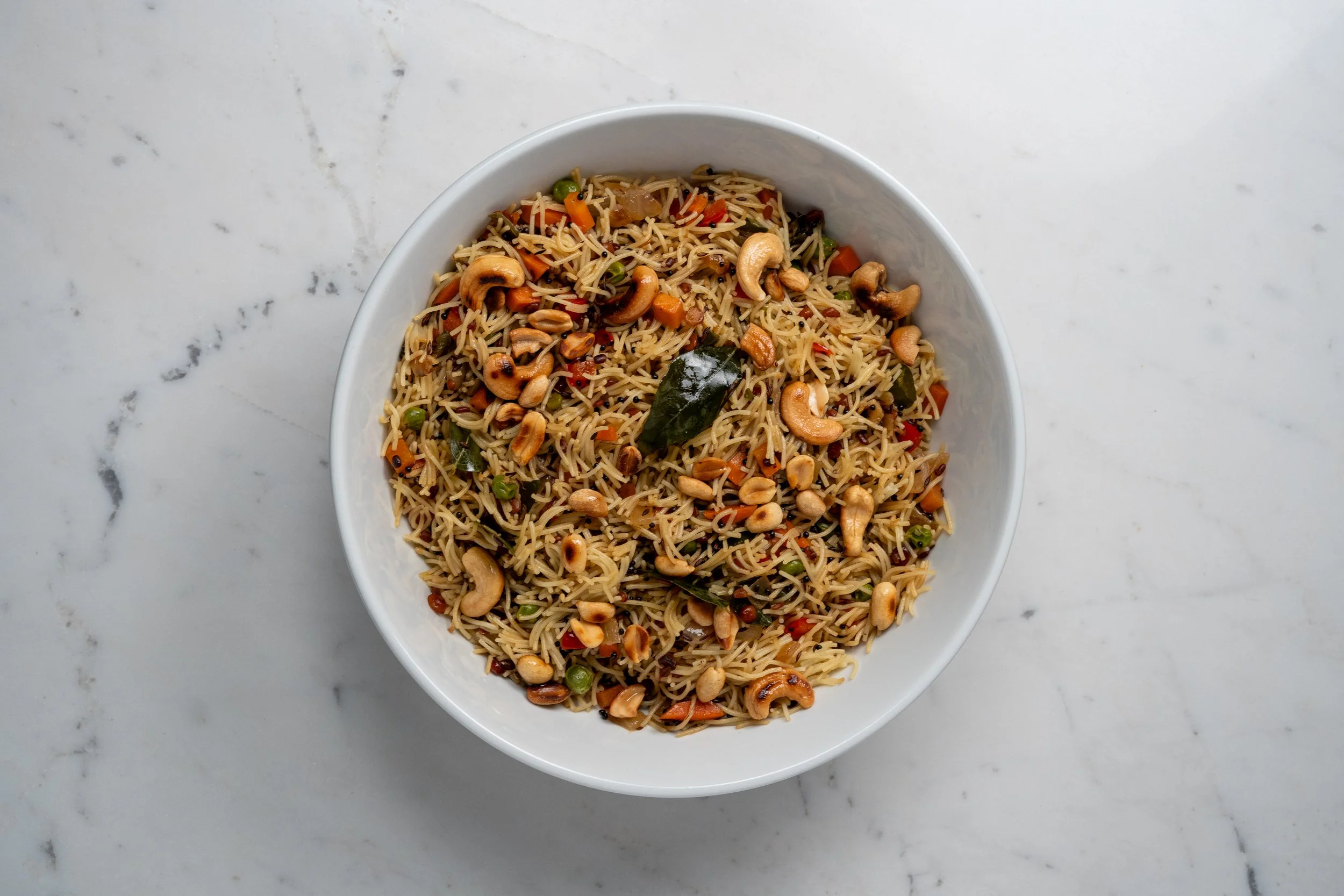 Ensalada de fideos con verduras y nueces en un tazón blanco sobre una mesa de mármol.