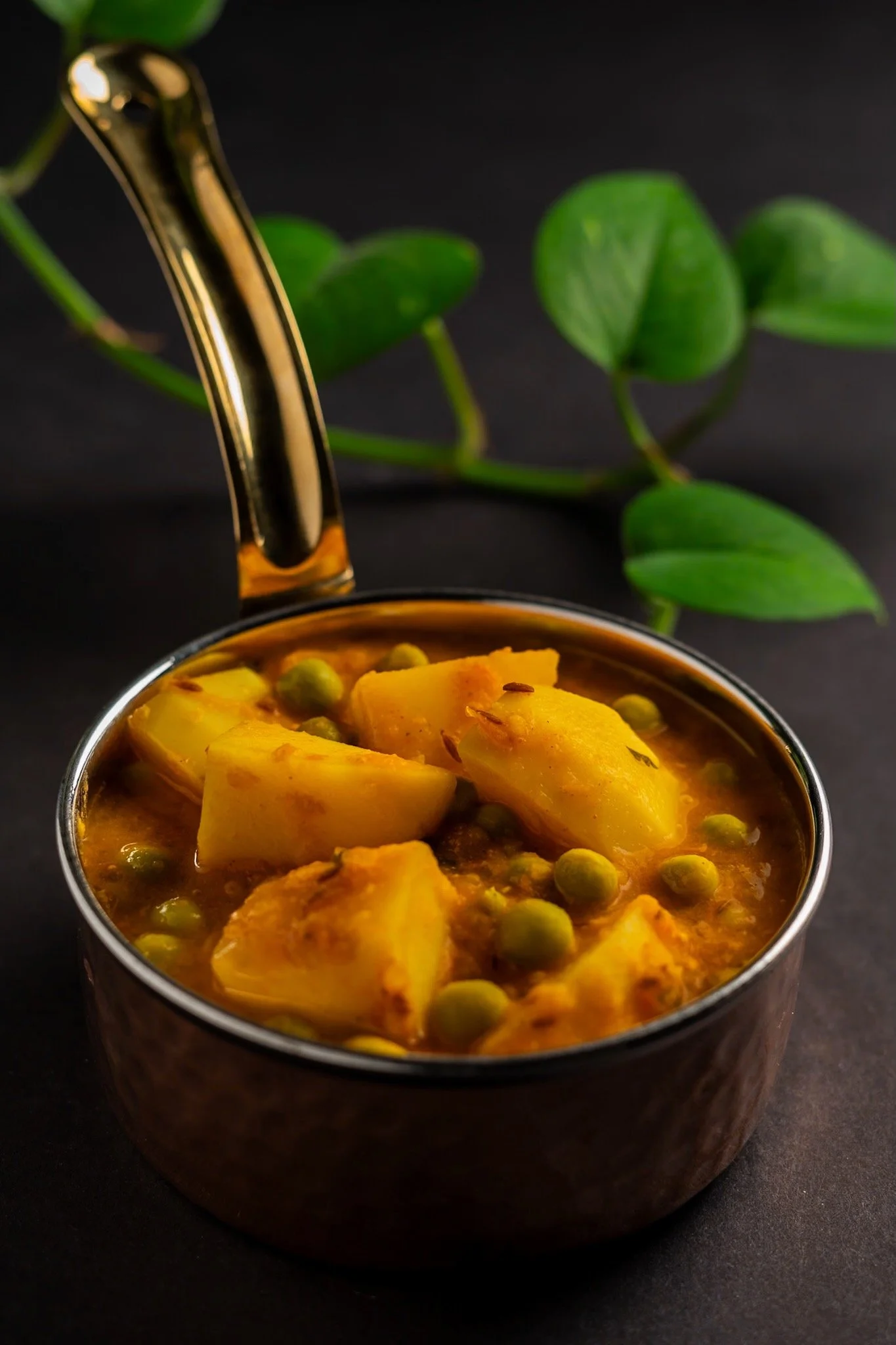 Vas de cerámica con sopa de papas y chícharos, con fondo negro y hoja verde.