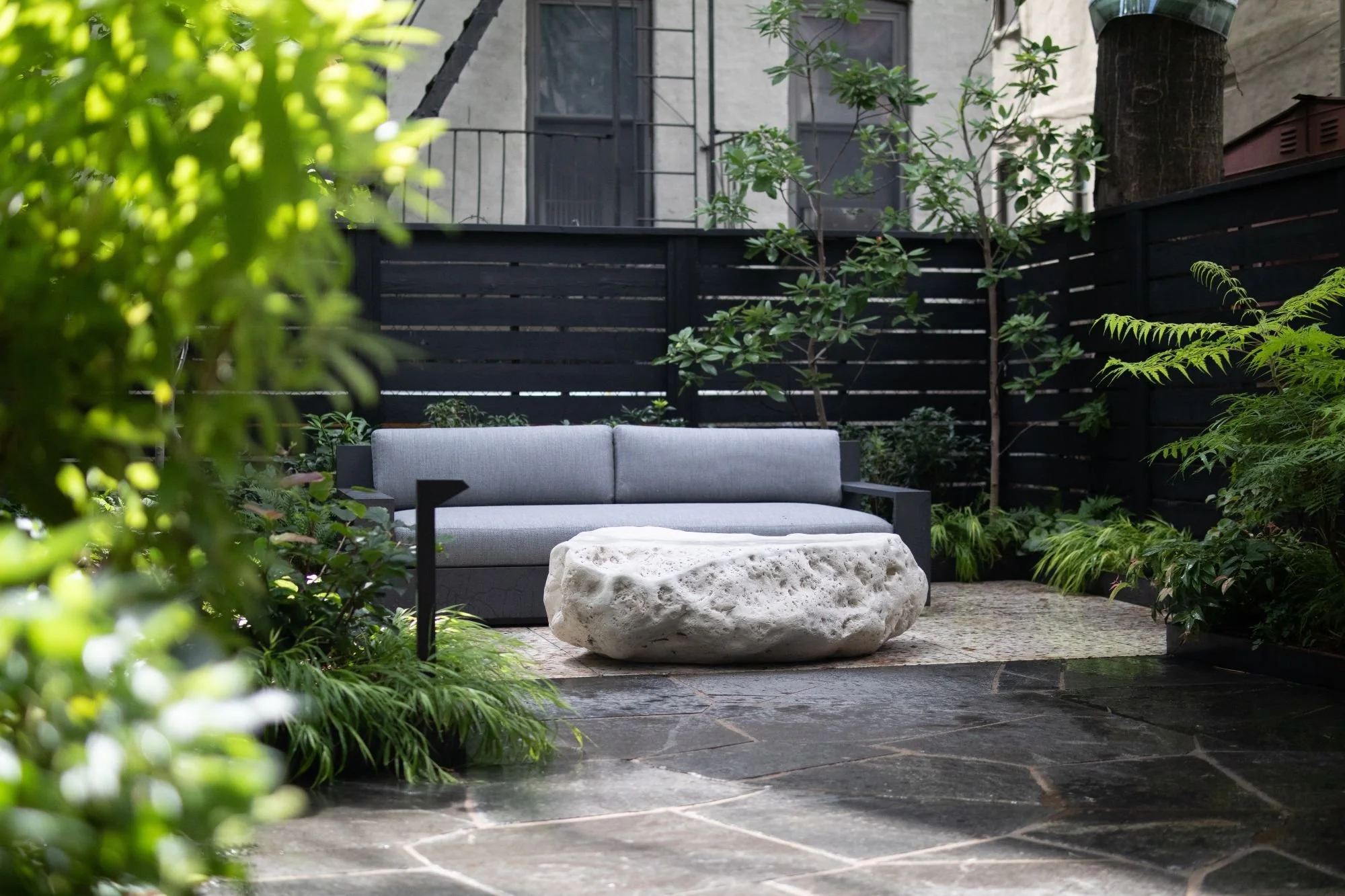Modern shade garden with natural stone paving, furniture, and stone sculpture 