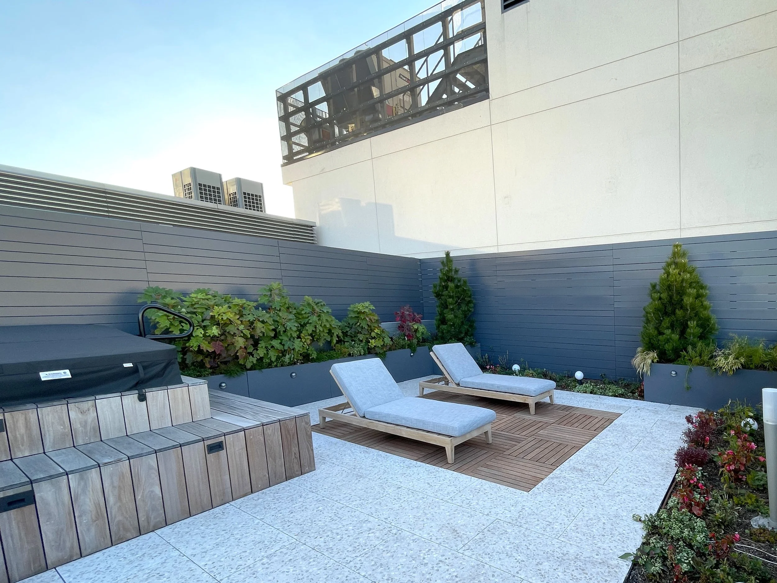 Rooftop lounge space with outdoor chaise lounge chairs and a hot tub with wood deck
