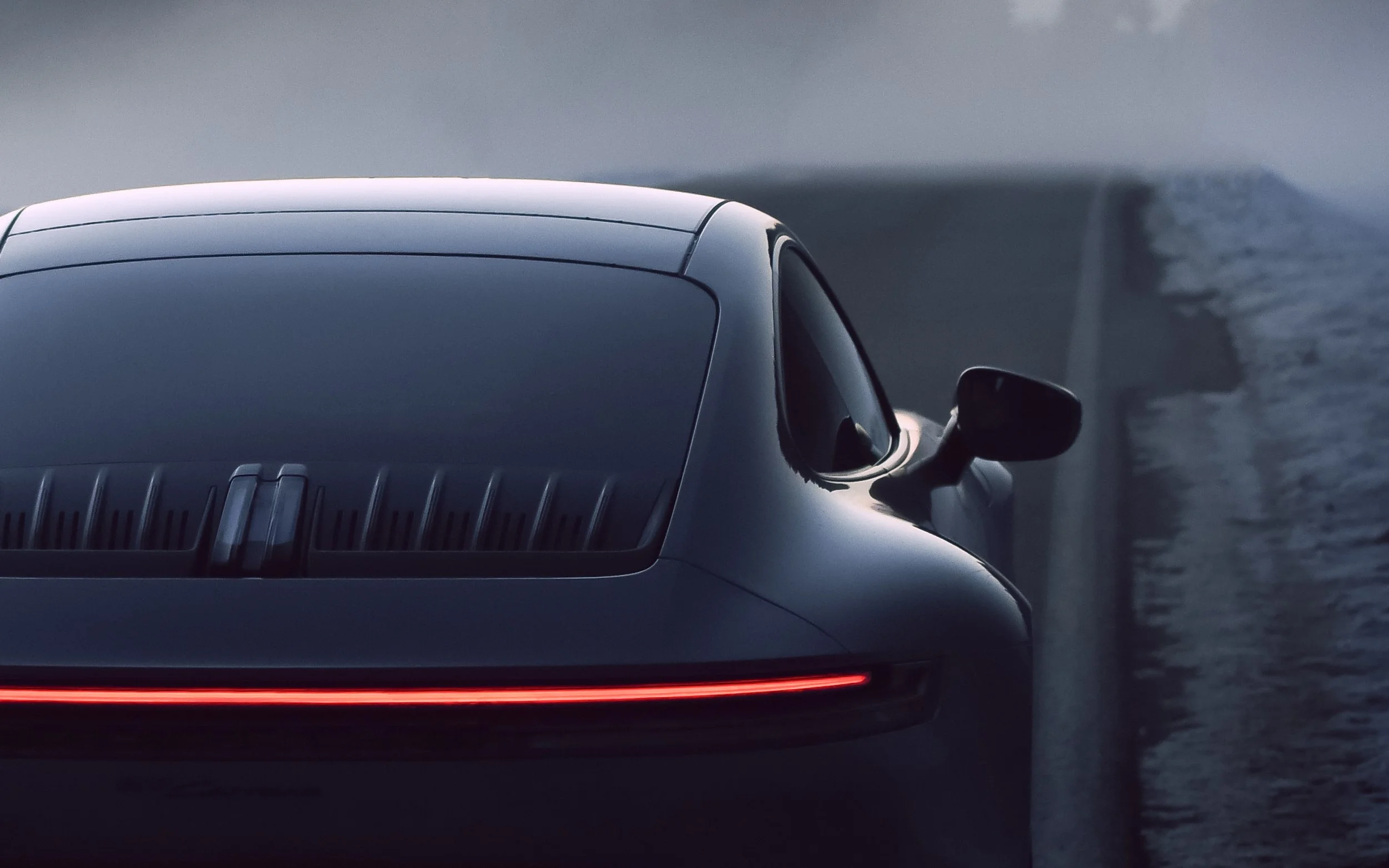 Close-up of a dark-coloredPorsche 911 Carrera  with a sleek design, parked near a body of water at dusk or dawn.