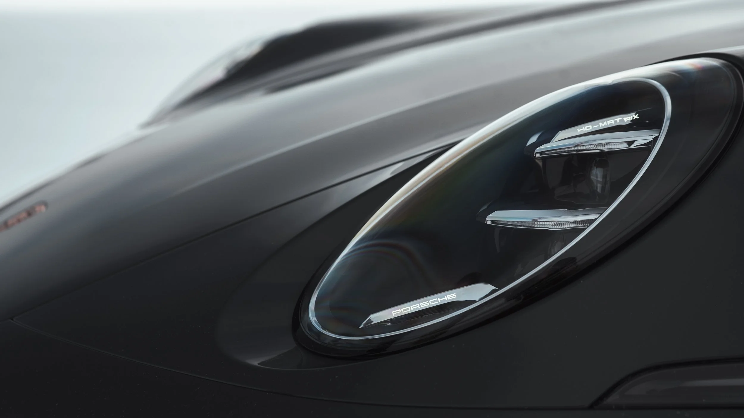 Close-up of a black Porsche 911 Carrera sports car headlight with the Porsche logo visible.