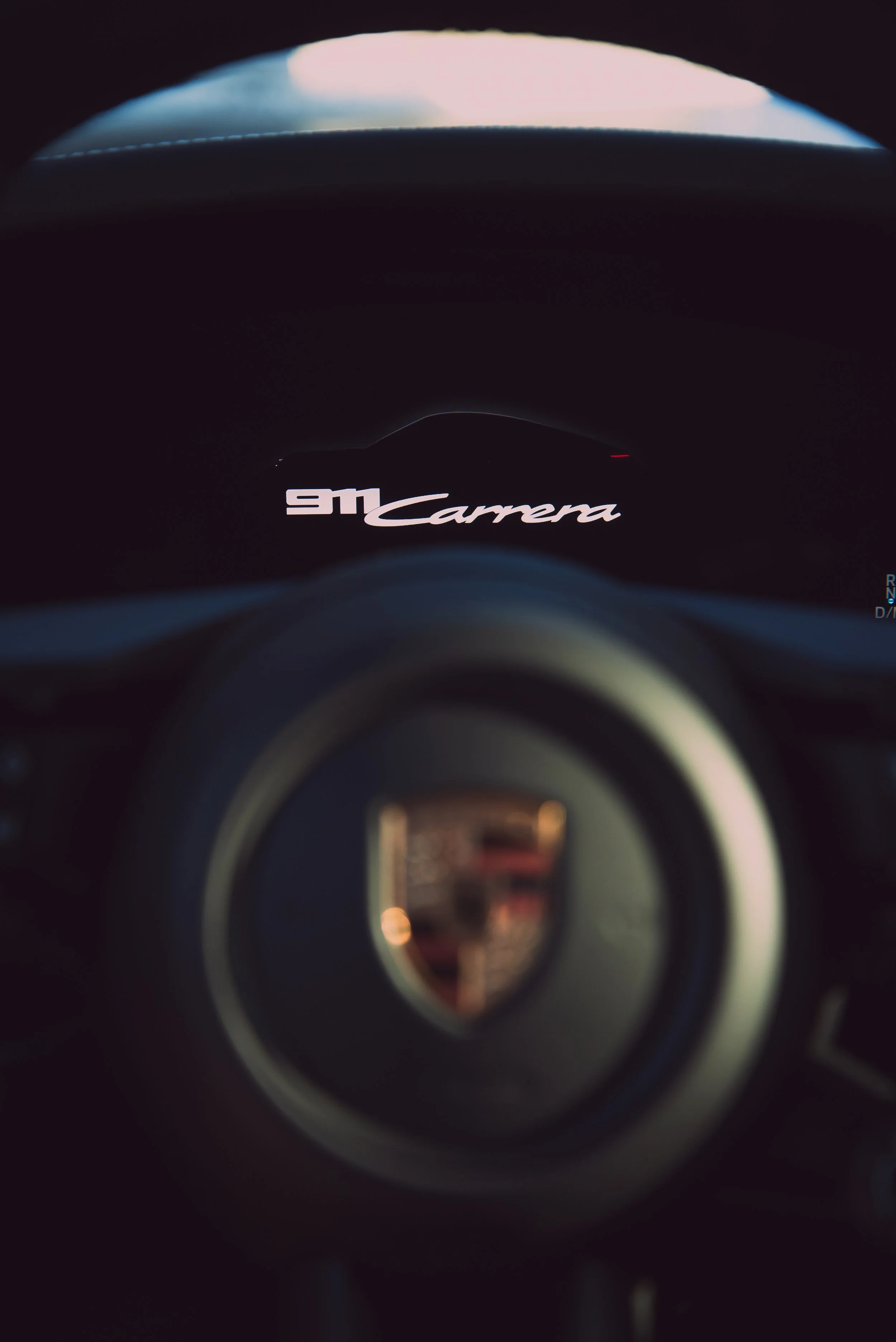 Close-up of a Porsche 911 Carrera dashboard with a focus on the digital display showing '911 Carrera' and blurred steering wheel.