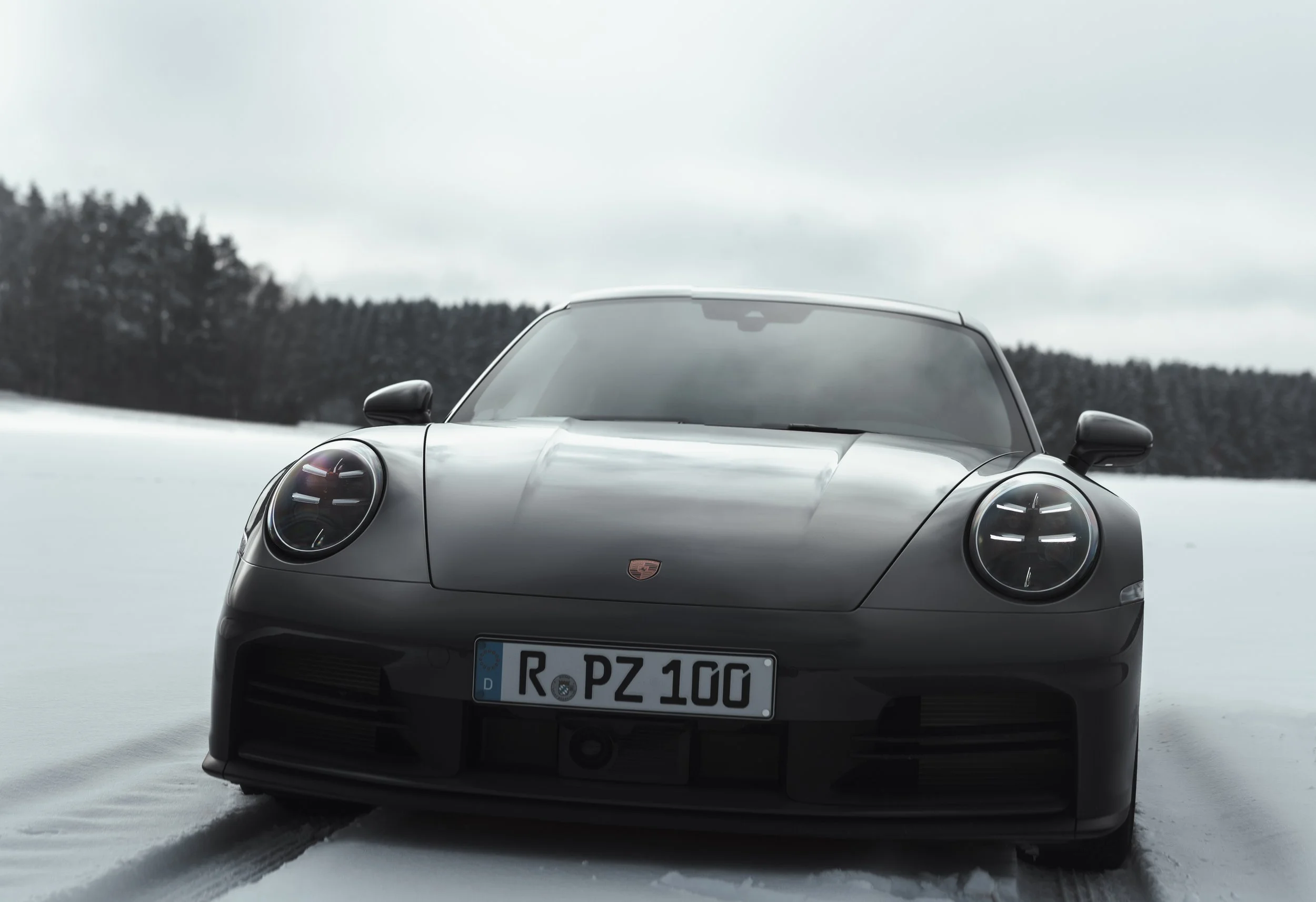 Front view of a sleek, blackPorsche 911 Carrera parked on snow with a forested background.