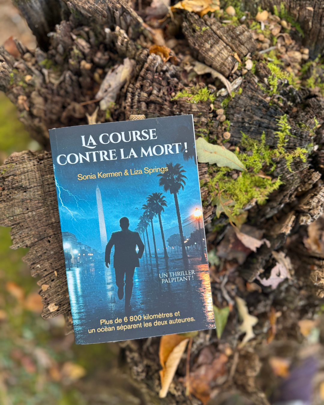 A paperback book titled 'La Course Contre La Mort!' by Sonia Kermen & Liza Springs, placed on a fallen tree trunk with moss and leaves, featuring a rainy night scene with a silhouette of a man running and palm trees in the background.
