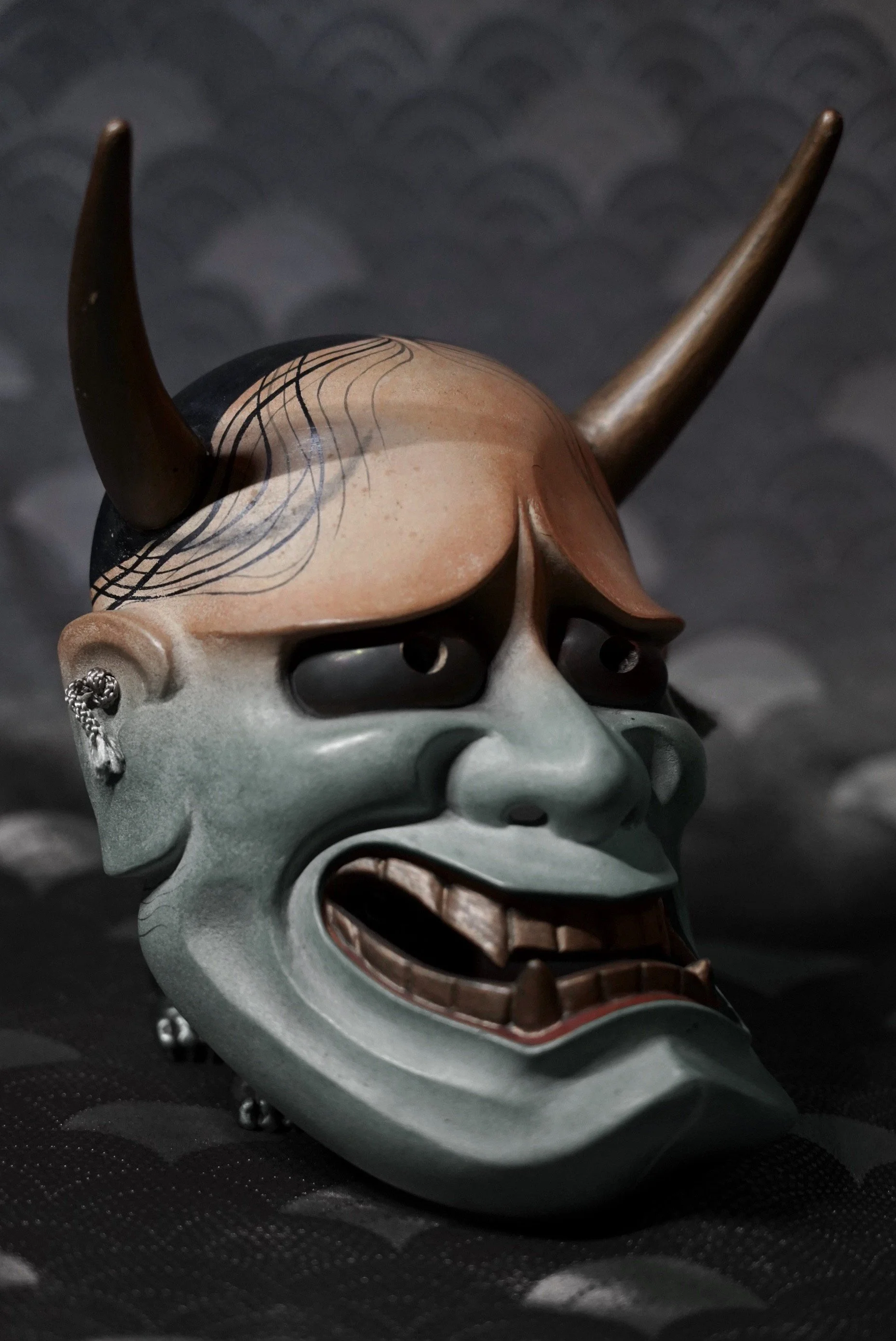 A detailed, artistic Hannya mask resembling a demon or Oni with large horns, a fierce expression and dark eye holes.