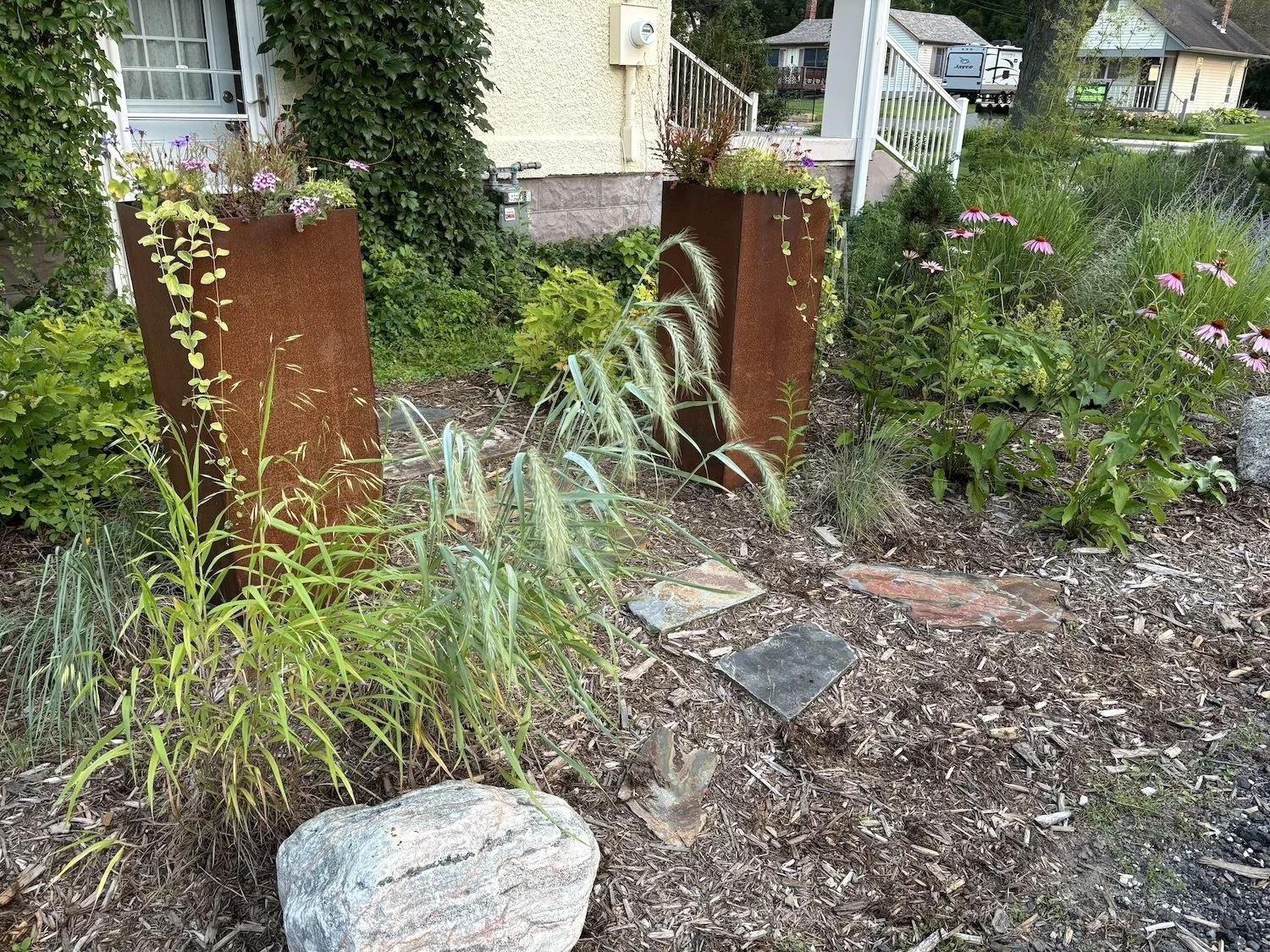 steel planters with natural boulders and native grasses, backdrop of formal vines