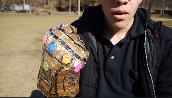 Person holding a decorated plastic bottle craft resembling a tiger, outdoors in a grassy area.