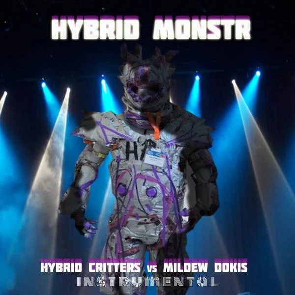 A person dressed in a homemade, monster-like costume with a wolf mask, standing on a stage with blue and white spotlights. The background features the text 'HYBRID MONSTER' at the top and 'HYBRID CRITTERS VS MILDEW DOKS INSTRUMENTAL' at the bottom.