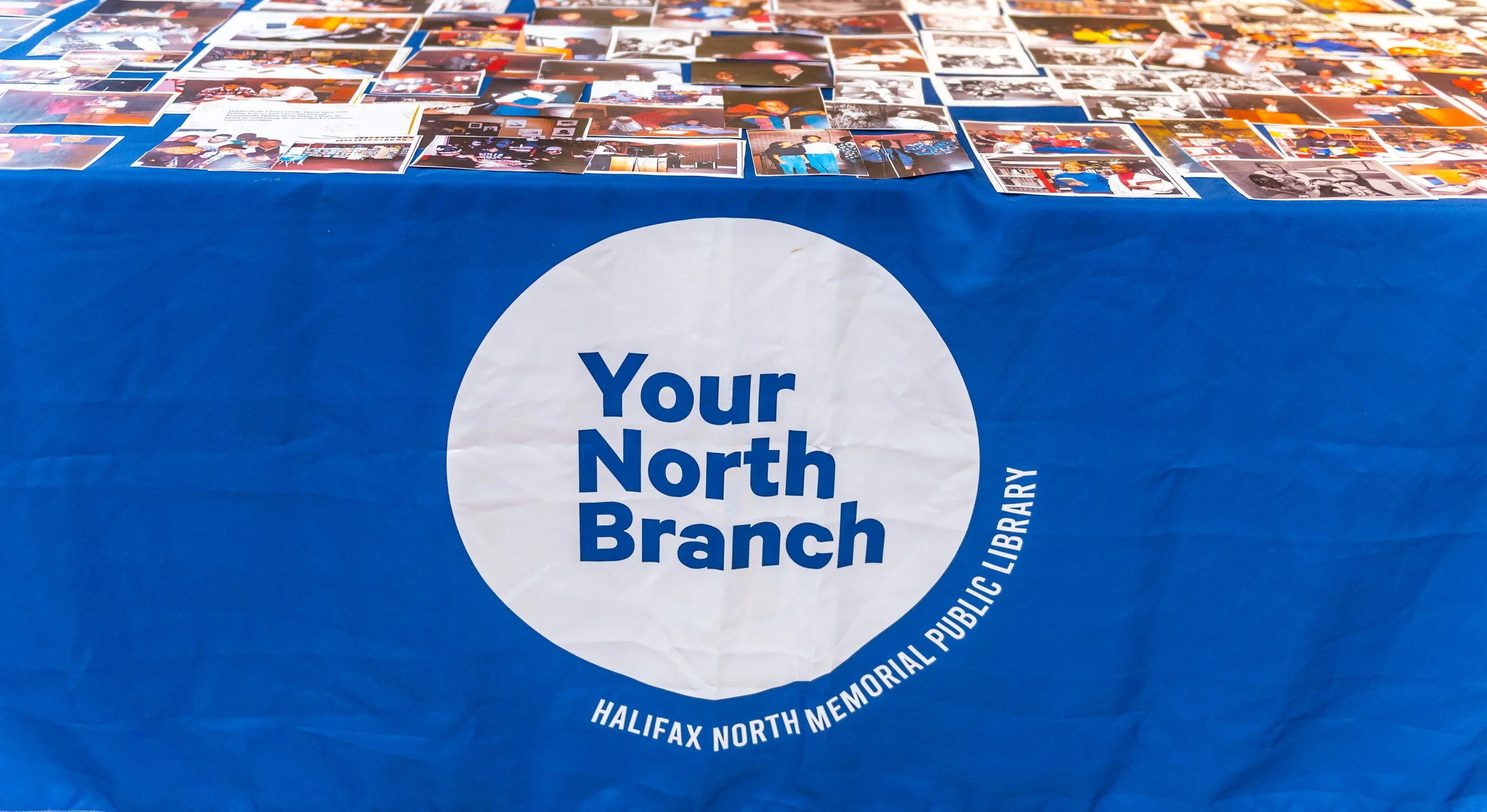  Table with a blue banner that reads “Your North Branch — Halifax North Memorial Public Library” with photographs all over the table. 
