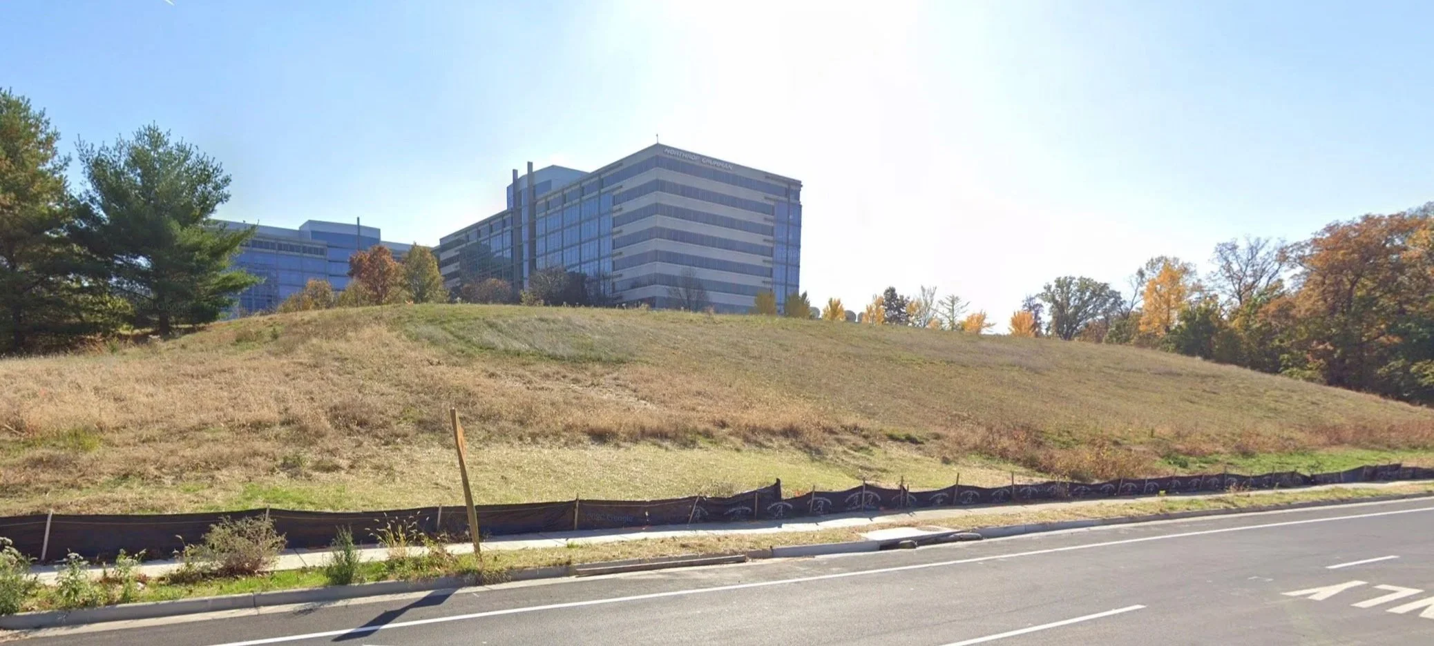 photo of a large grassy hill next to a road, with high rise office buildings in the background