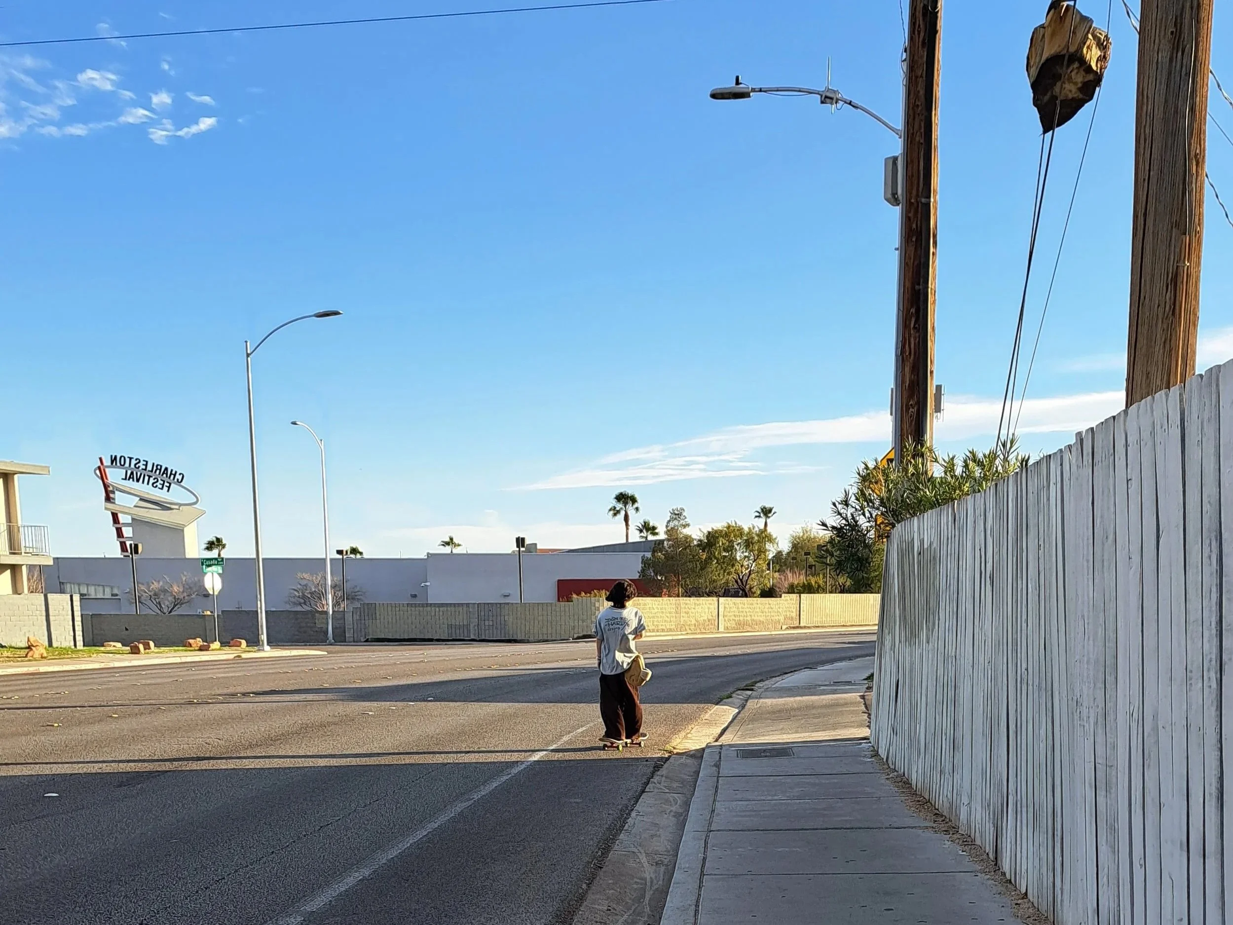 photo of a wide empty road in charleston, with a narrow sidewalk and painted line for a bike lane, with one person skateboarding on the road. there is no street life and the street is lined with fences