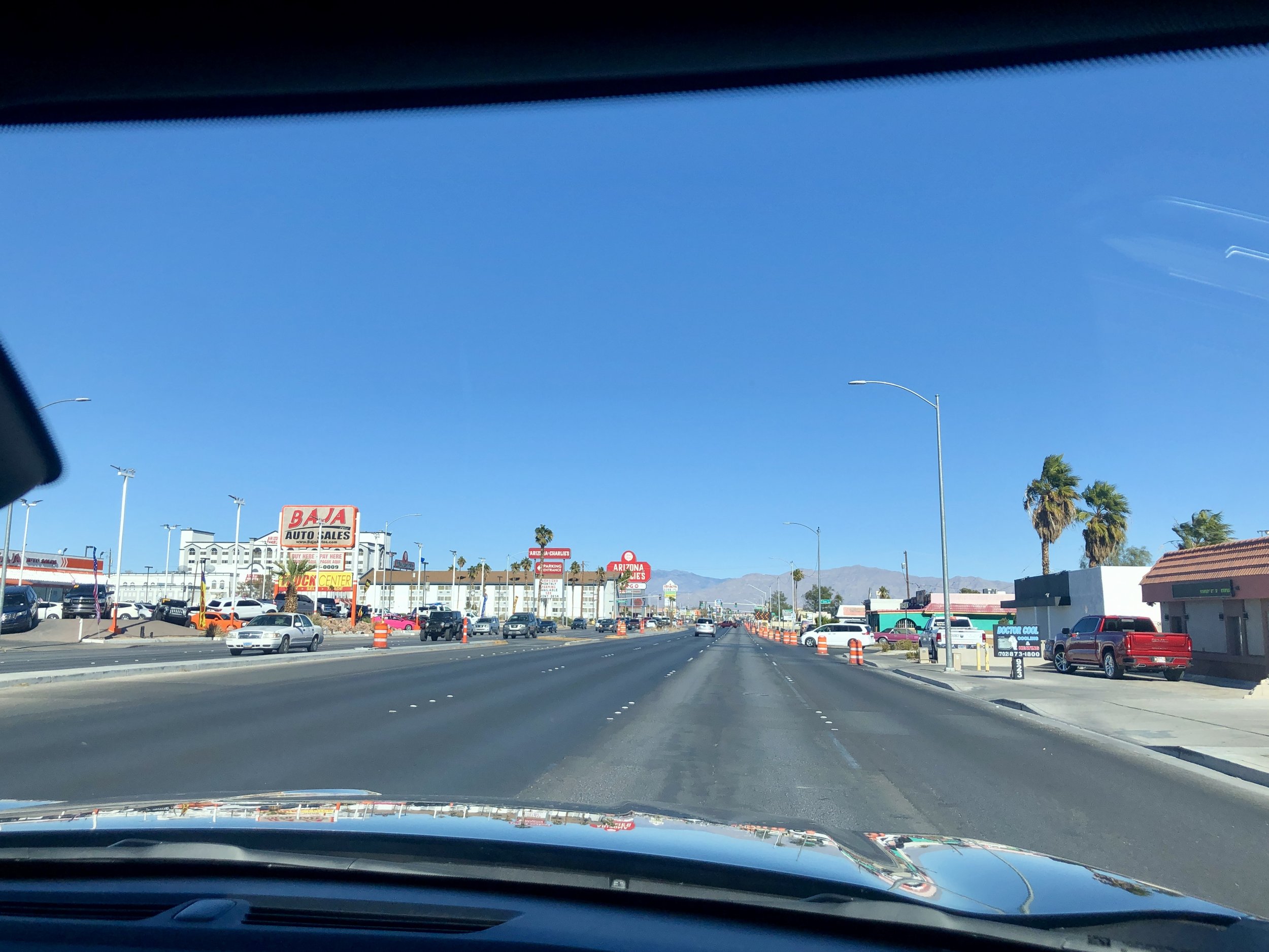 Photo from inside a car driving down a major road in Charleston, with 4 lanes of traffic in each direction. The road is not very full of cars, and lined with driveways to parking lots and strip mall developments. there is no shad and minimal sidewalk
