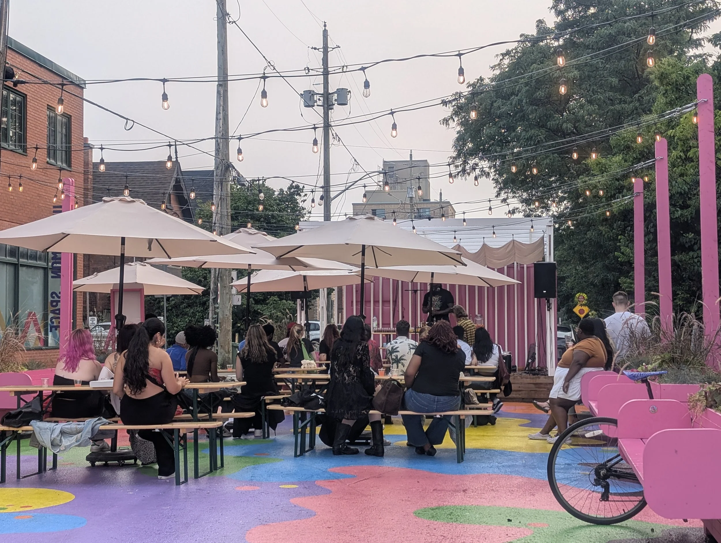 Photo of the Florence St activation with people sitting at picnic tables under umbrellas in the plaza, with a colourful mural on the ground