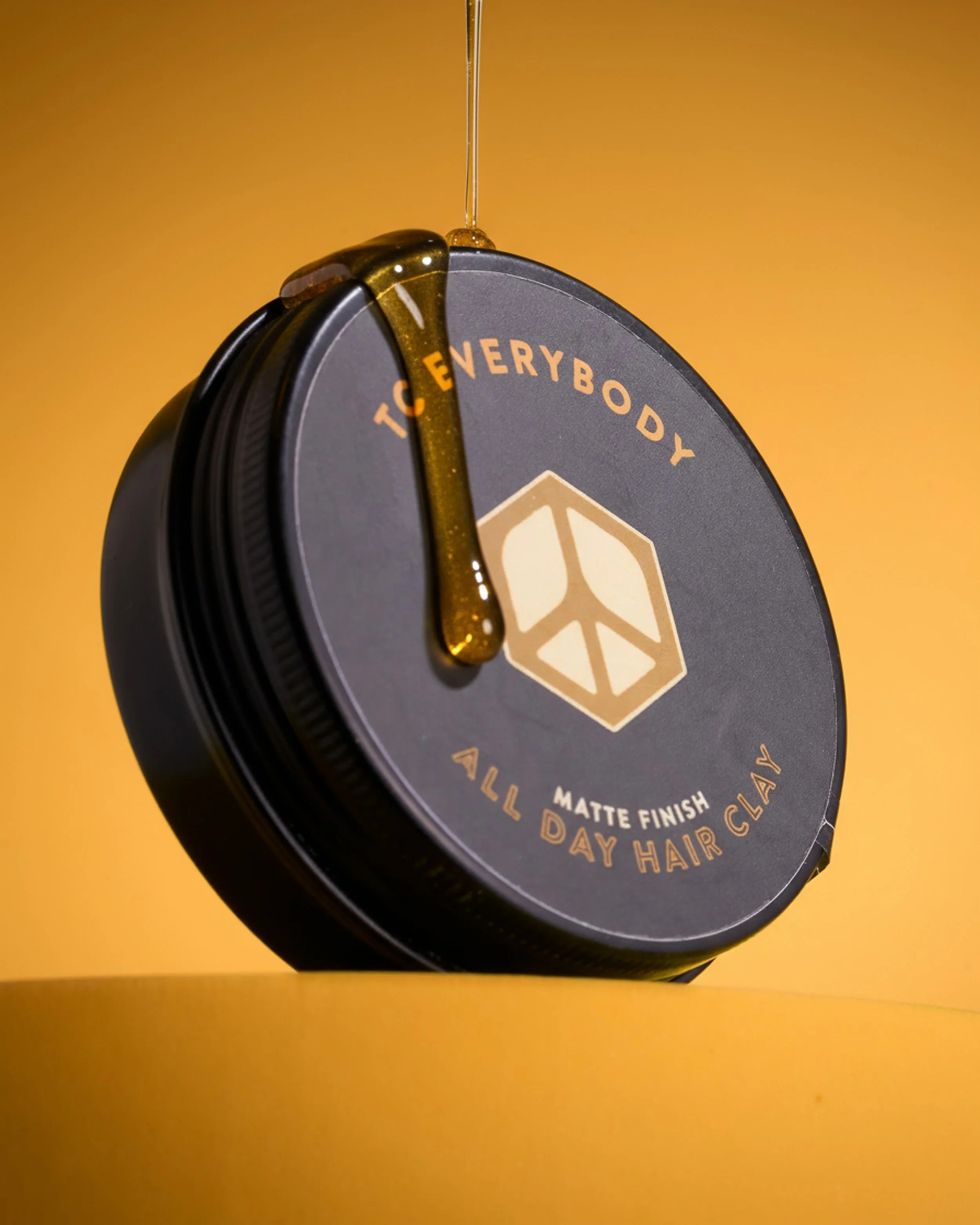 Container of TC Everybody all day hair clay with matte finish on a wooden surface.