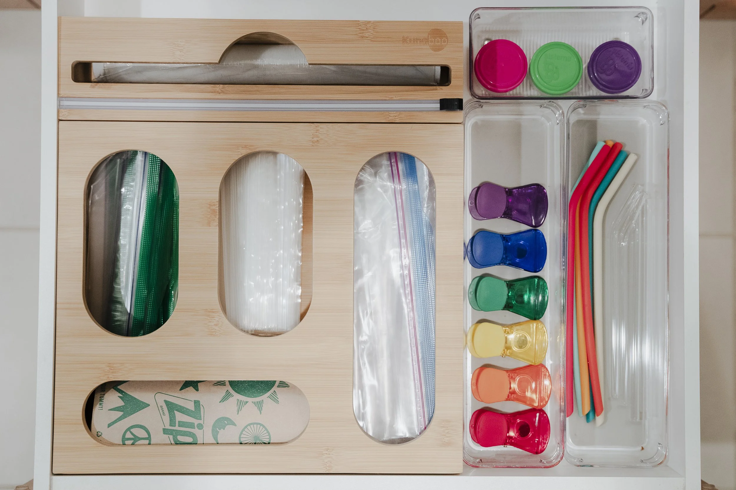 A wooden tray with multiple ziplock bags, small colorful cups, straws, and silicone lids organized in compartments.