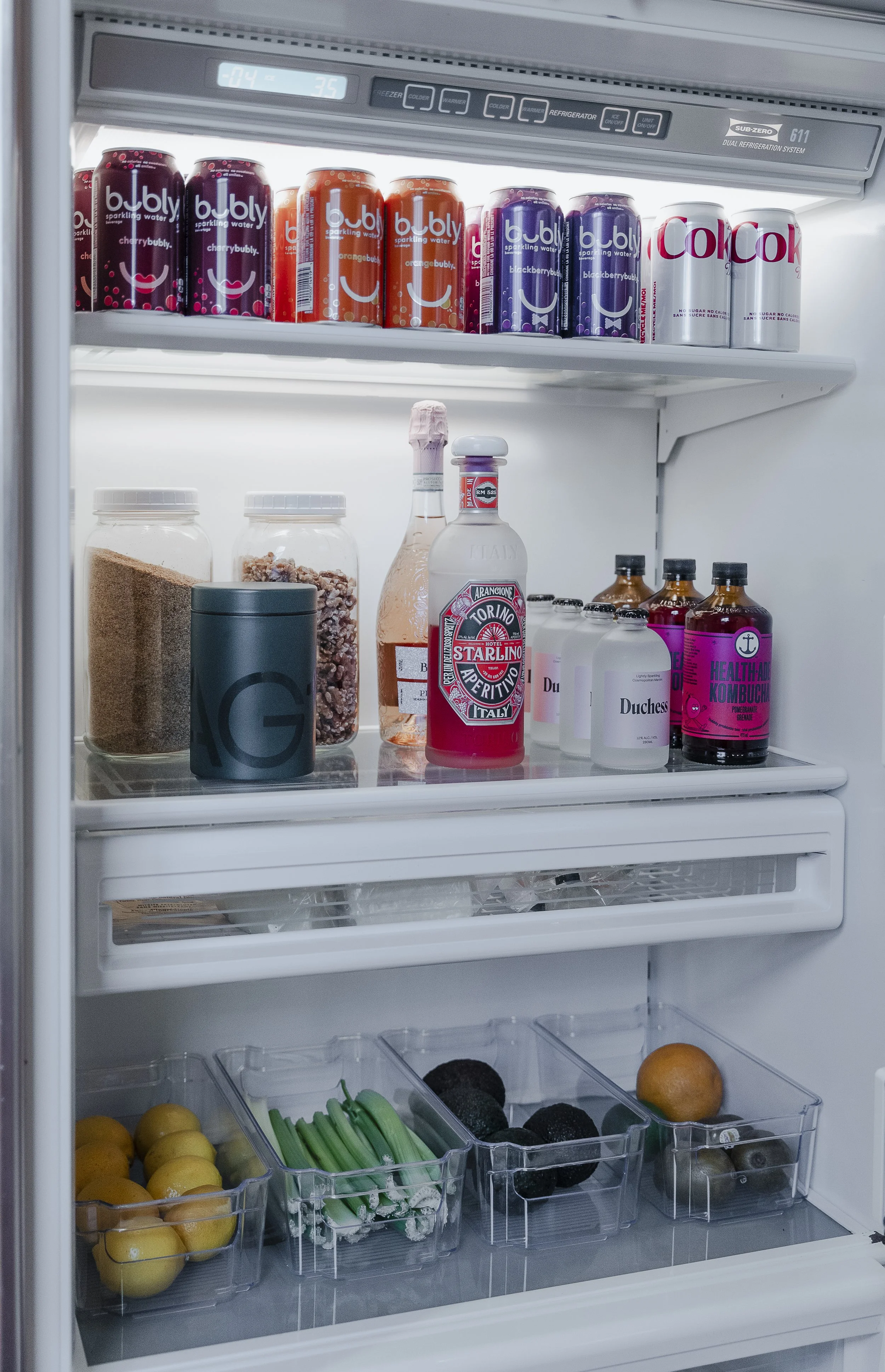 Inside of a refrigerator with various beverages, condiments, and fruits on shelves.