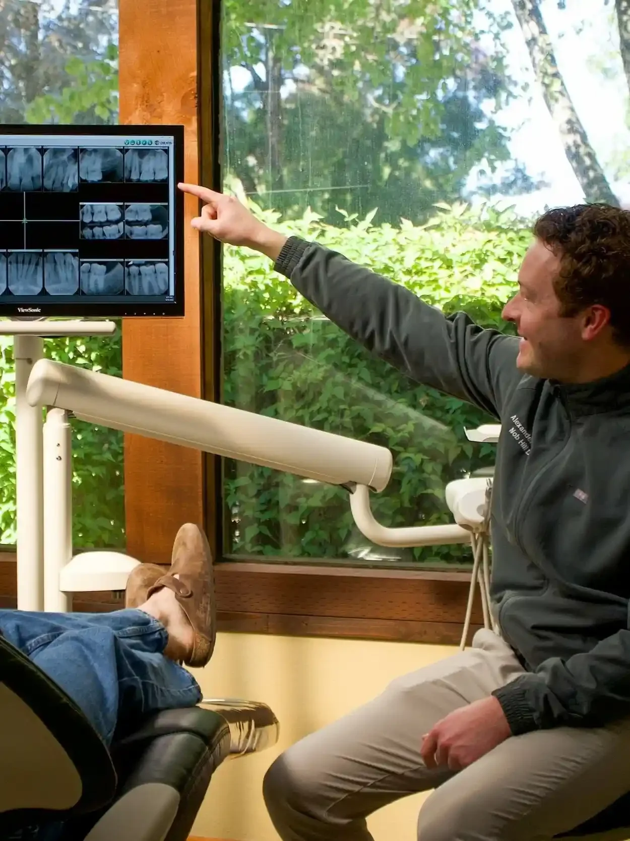 Dentist pointing to a dental X-ray on a monitor during a patient consultation