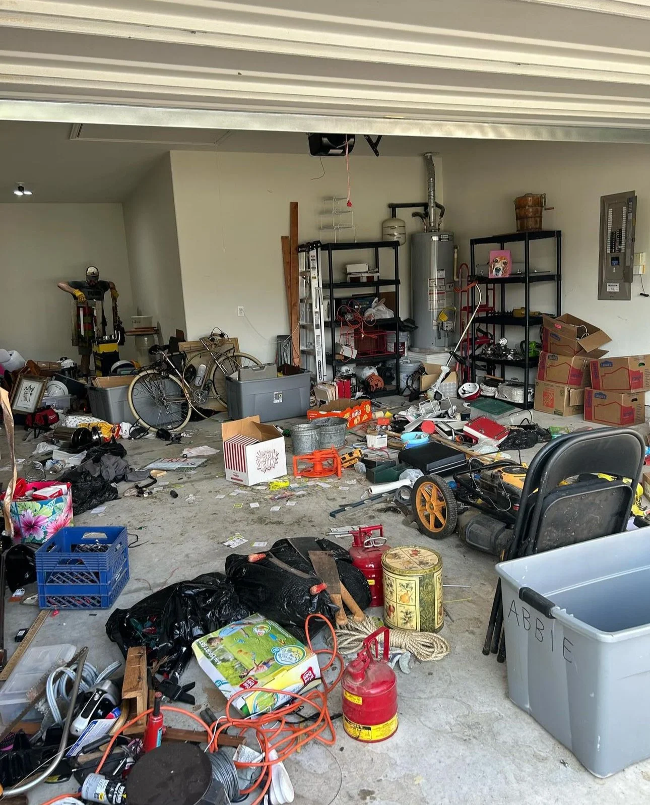 Disorganized garage with clutter including boxes, tools, bicycles, and storage shelves.