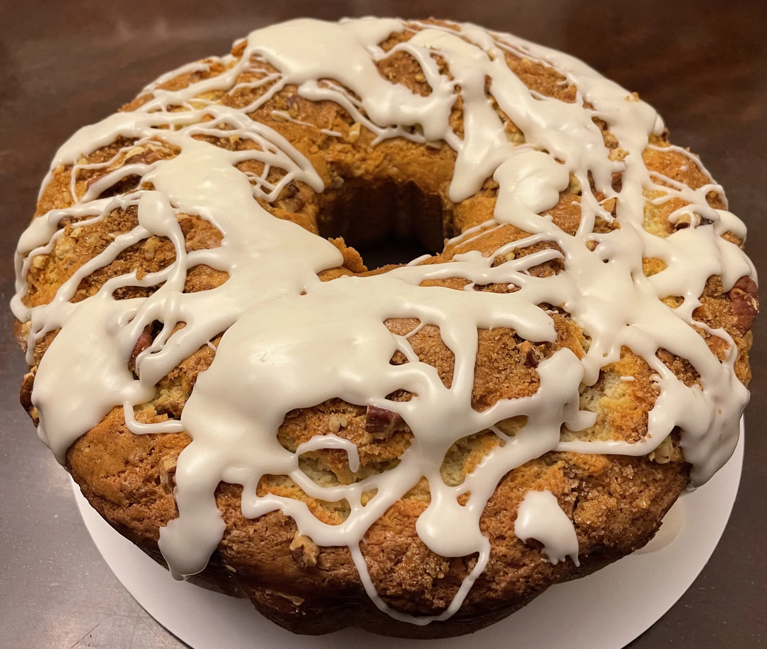 A coffee cake bundt cake with white icing drizzled on top, placed on a white plate.
