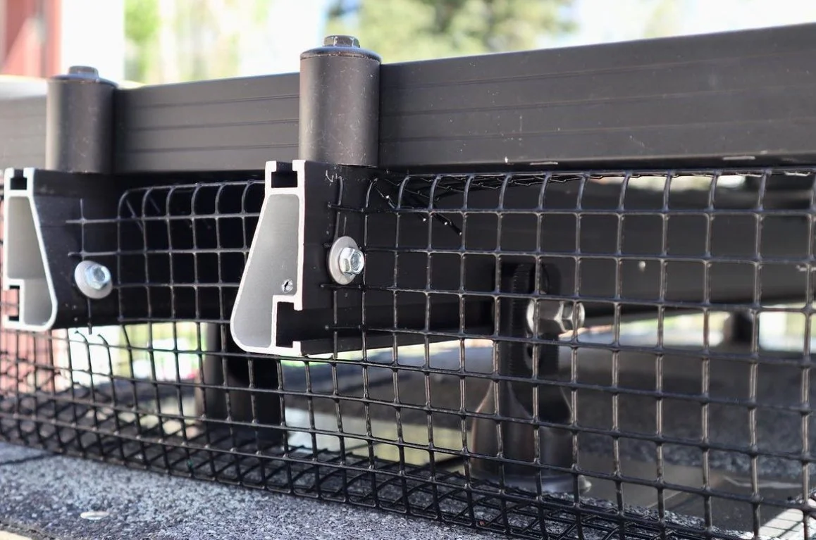 Close-up of metal mesh fencing attached to a black structure with bolts and brackets.