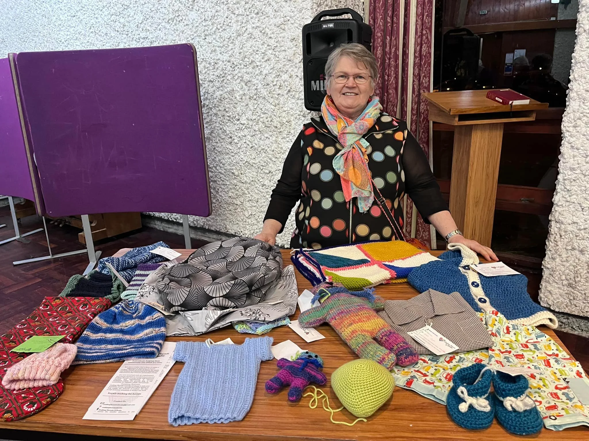 Kay smiles from behind a table of crafted items