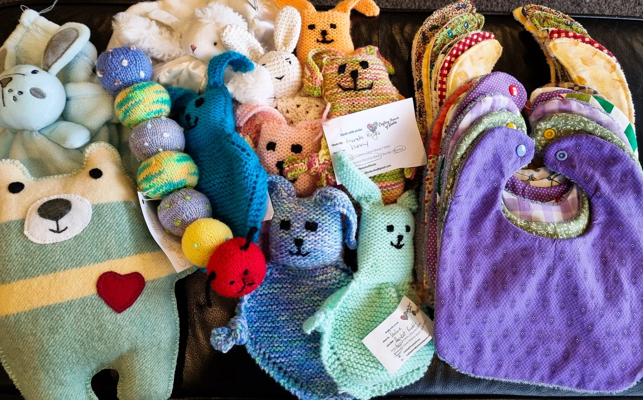 A table of knitted animals, lovies, and baby bibs