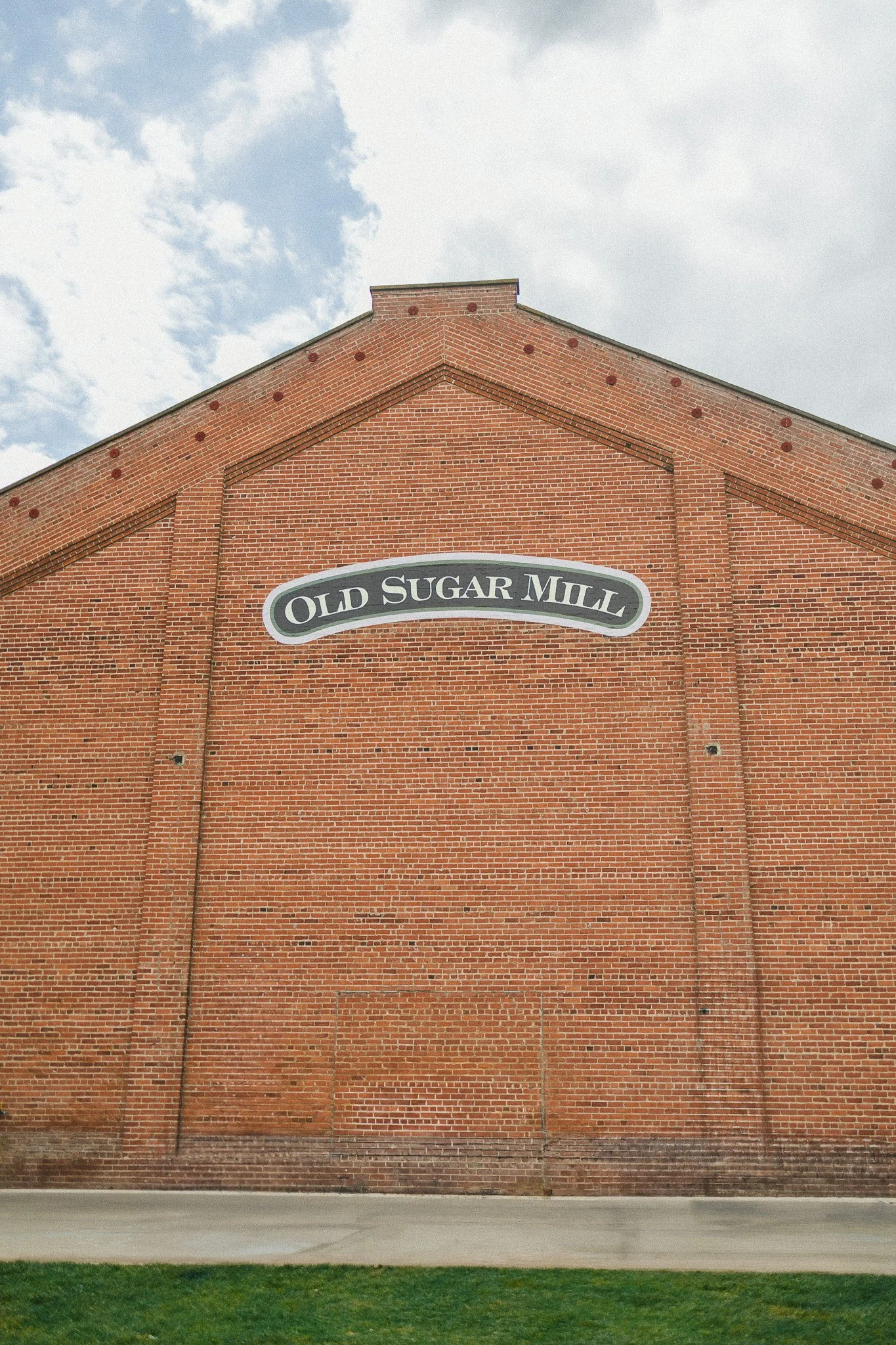 Brick building with a sign that reads 'Old Sugar Mill' against a cloudy sky.
