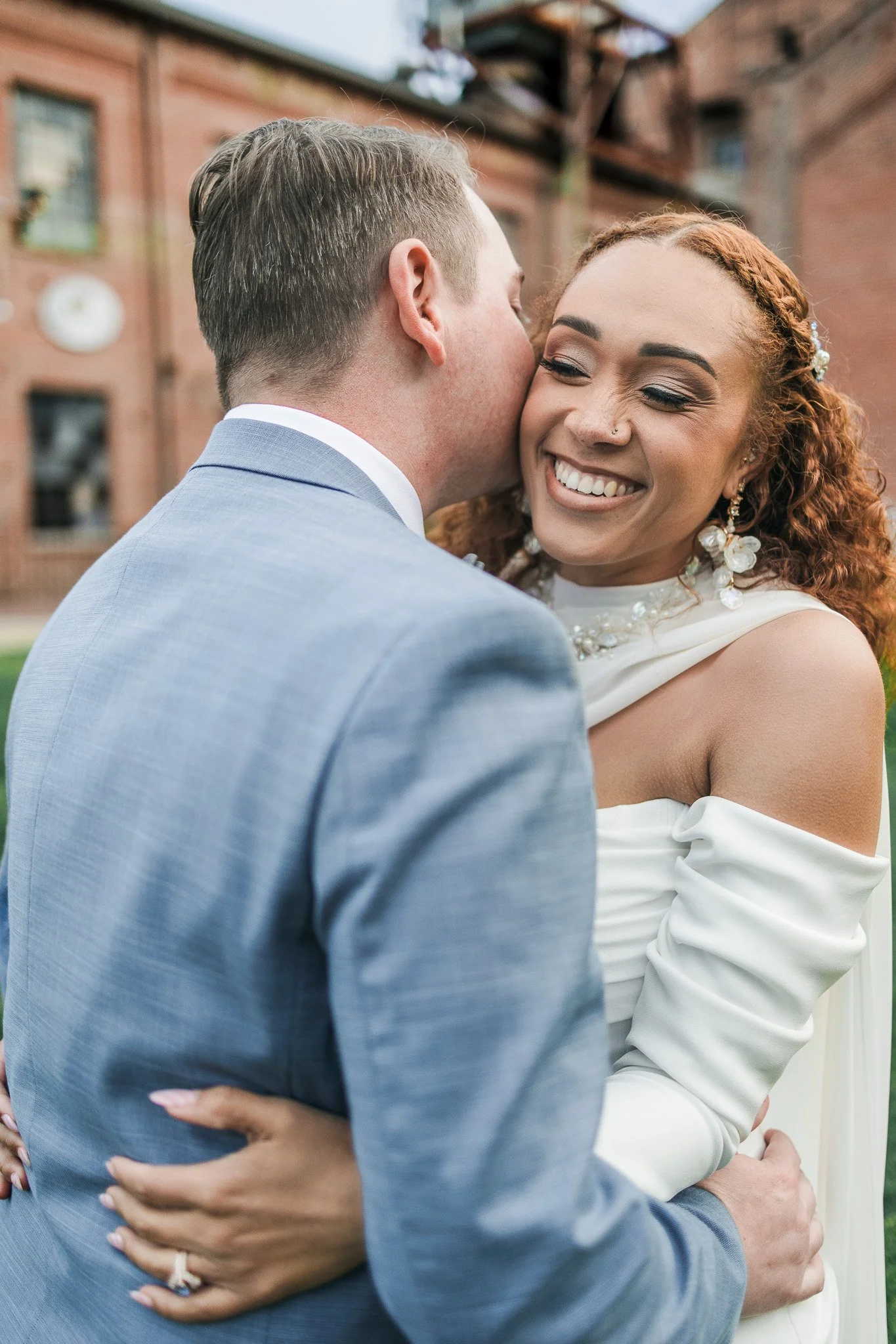 A bride and groom sharing a kiss outdoors, smiling.