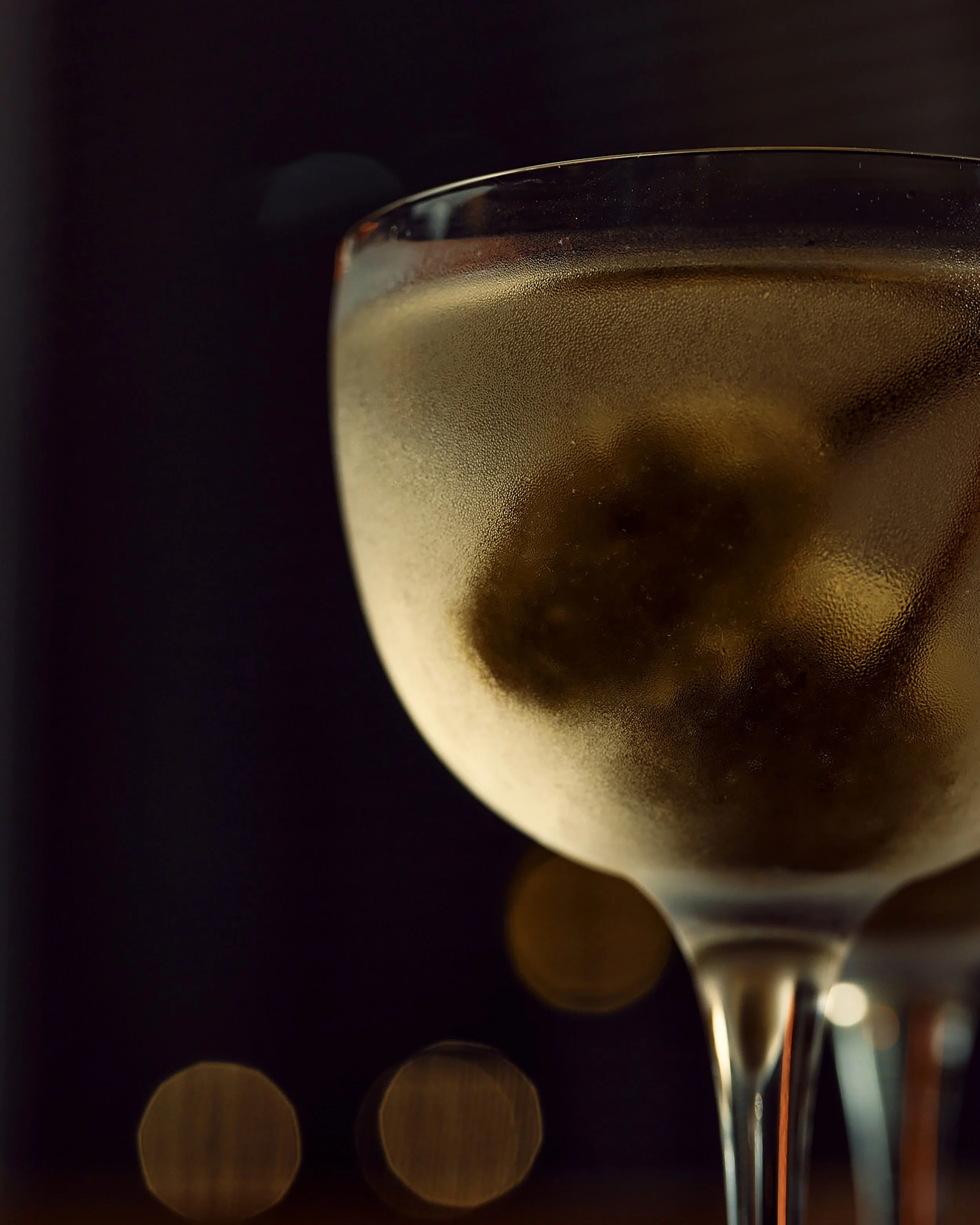Close-up of a glass of champagne with ice cubes against a dark background with bokeh lights.