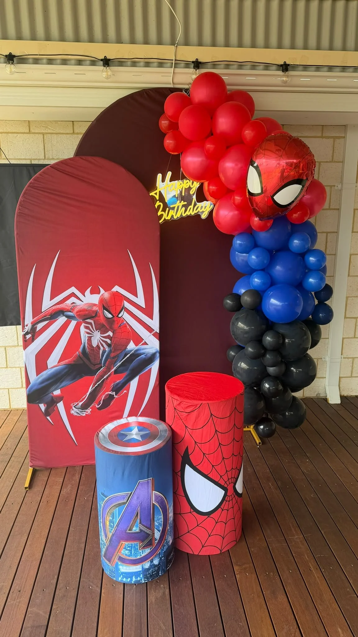 Spider-Man themed birthday decoration with balloons, backdrop, and themed pillars on a wooden floor.