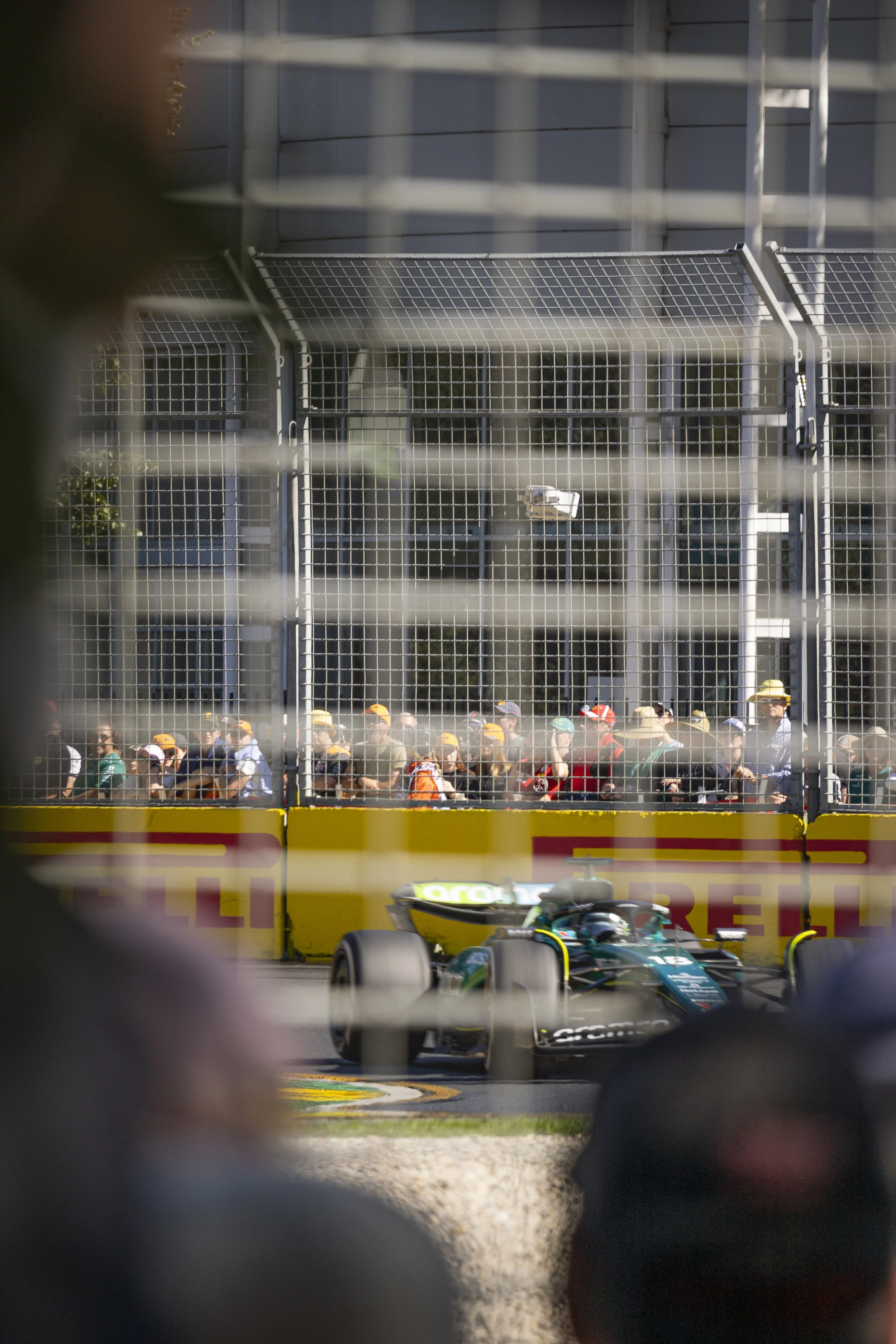 A race car driving past a crowd of spectators separated by a safety barrier at a motorsport event.