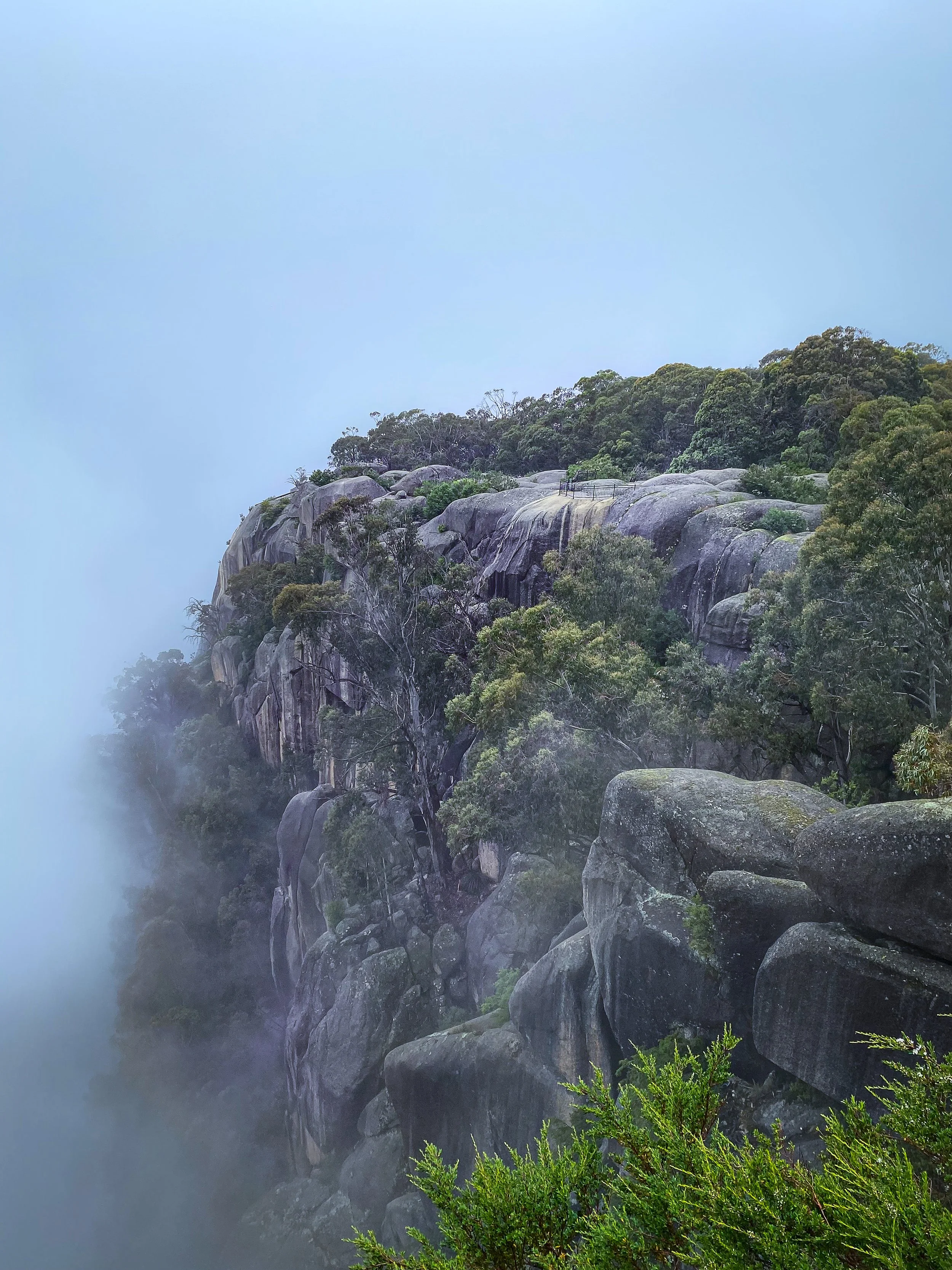 A misty mountain landscape with large rocks, green trees, and a cloudy sky.