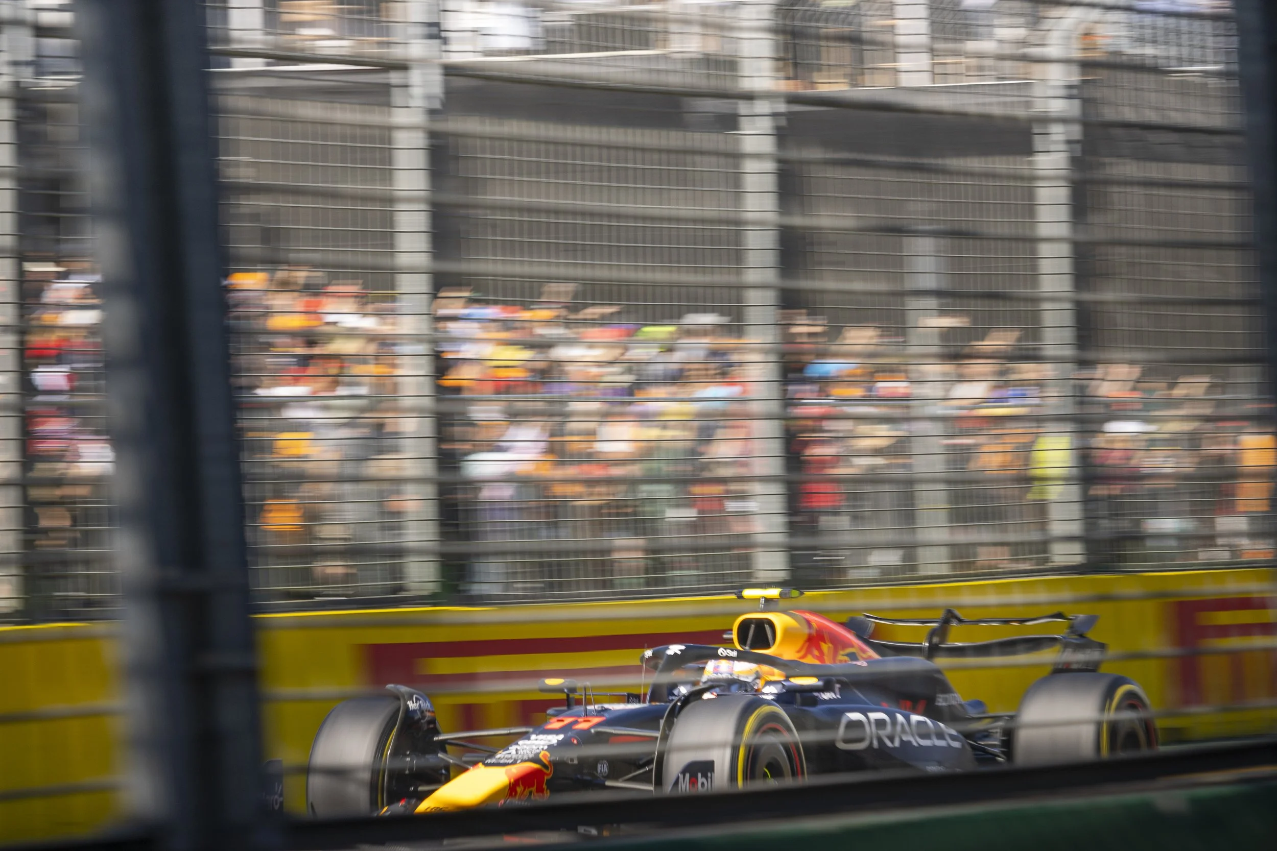 A Formula 1 race car on the track behind a safety barrier, with blurred crowd in the background.