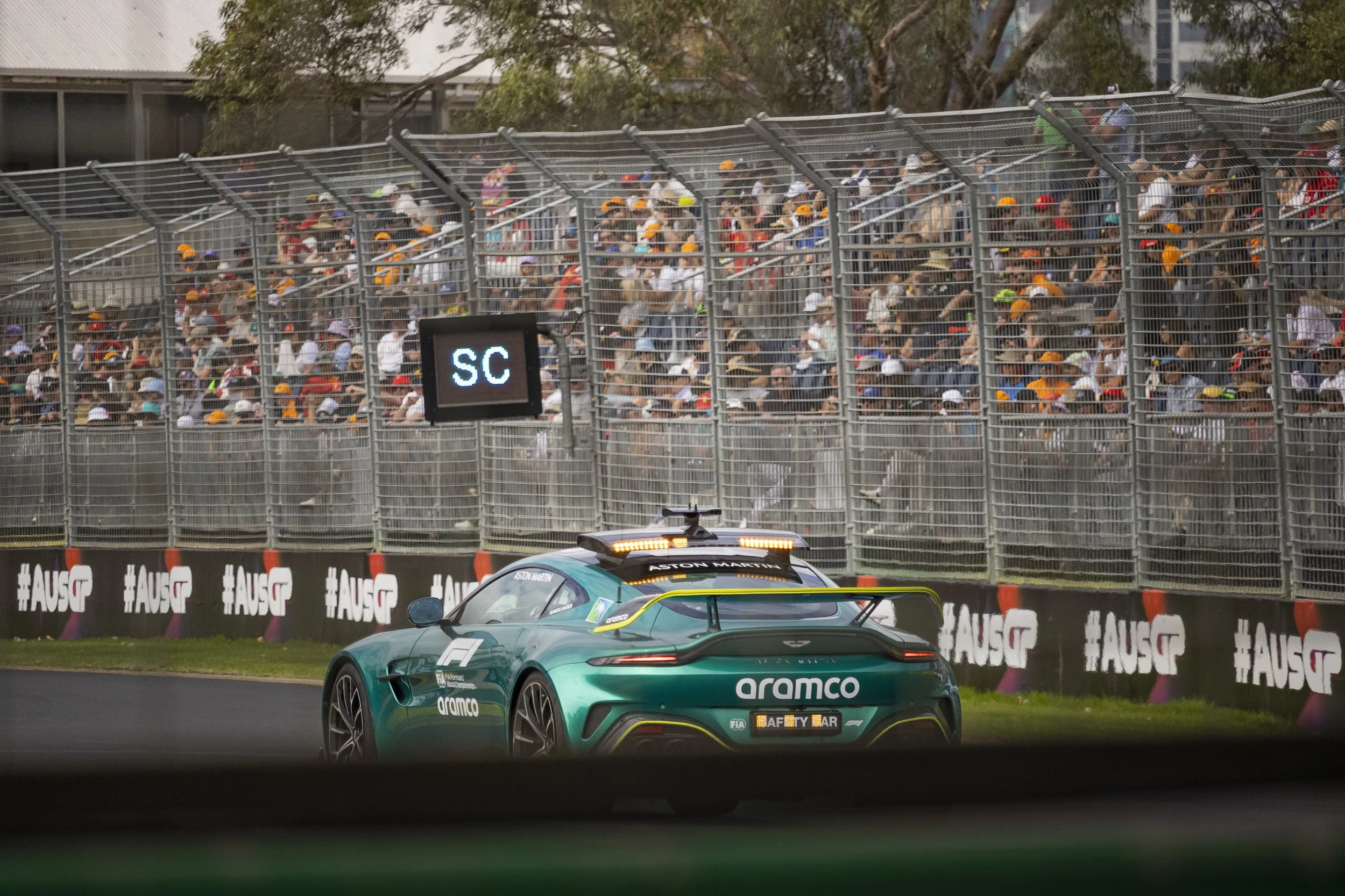 A green Aston Martin race car on a race track with a large crowd of spectators behind a safety barrier.