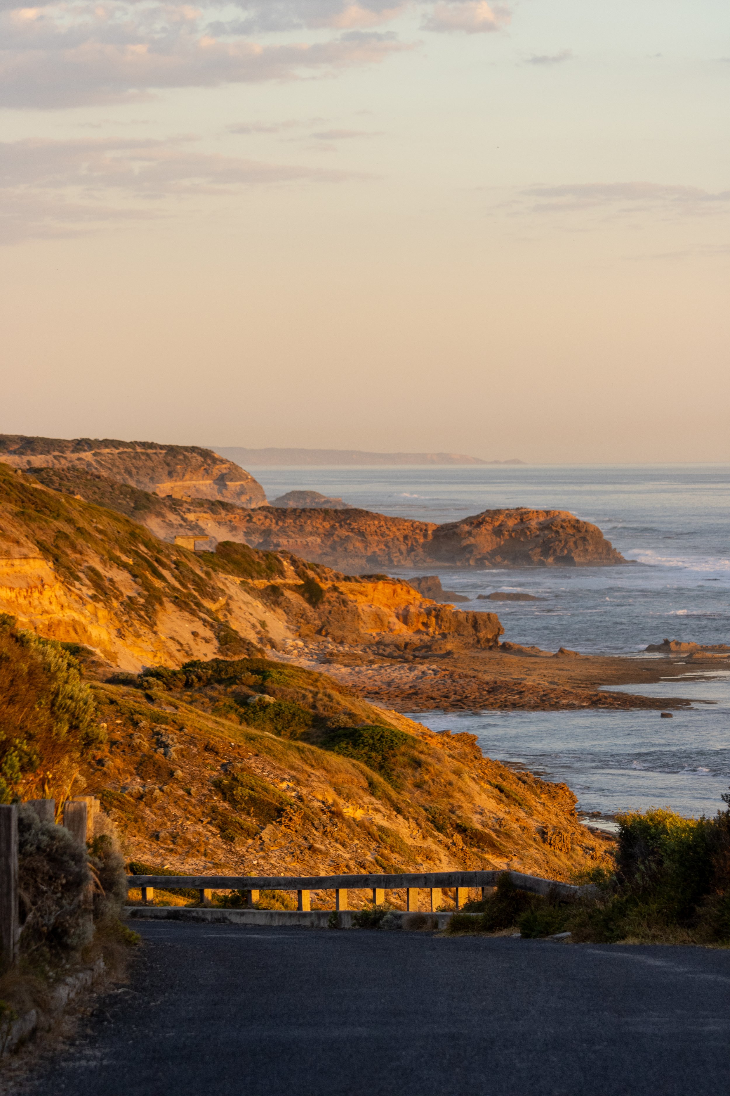 Coastal cliffs at sunset with a winding road in the foreground and ocean waves crashing on the shore.