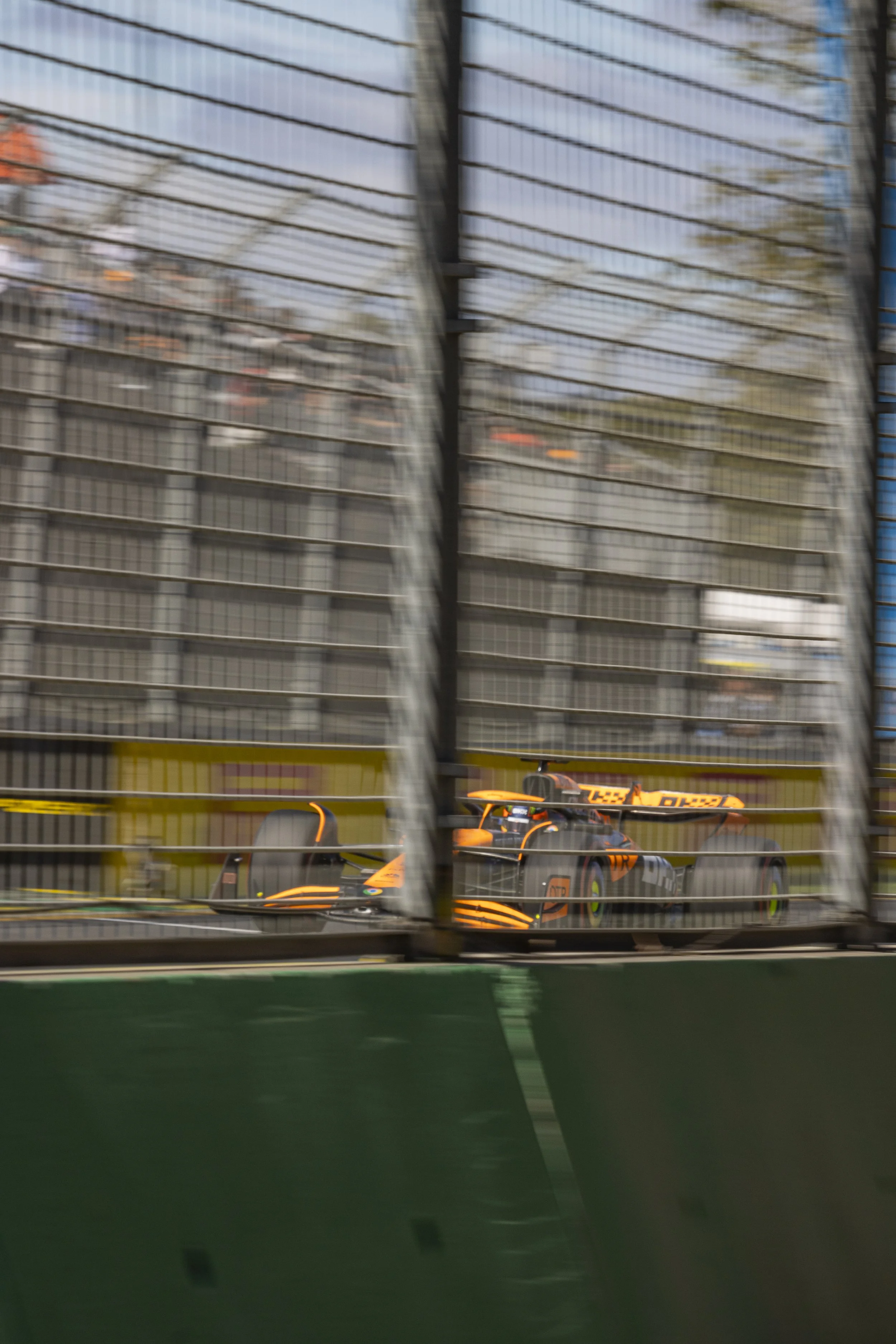 Race car on track behind a safety barrier, seen through a wire fence.