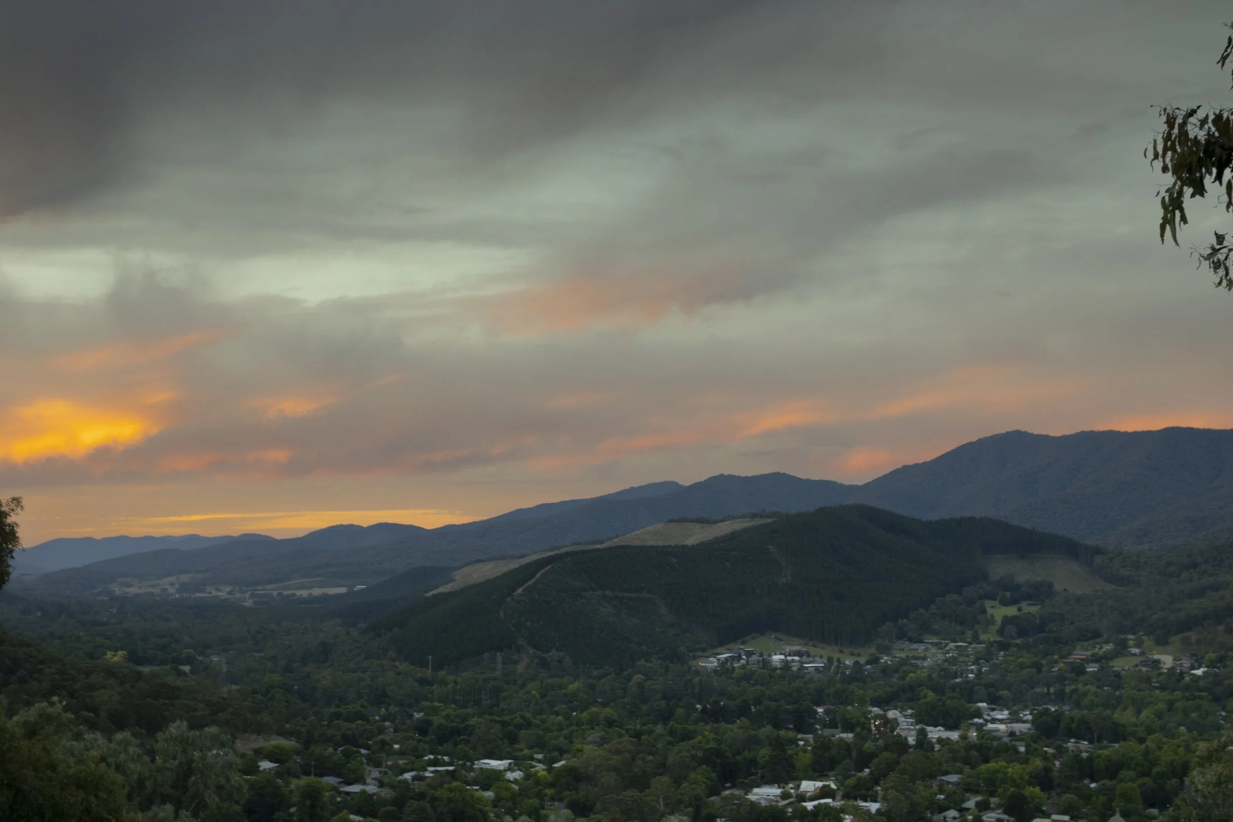 Scenic view of mountainous landscape during sunset with a cloudy sky and a small town at the base of the hills.